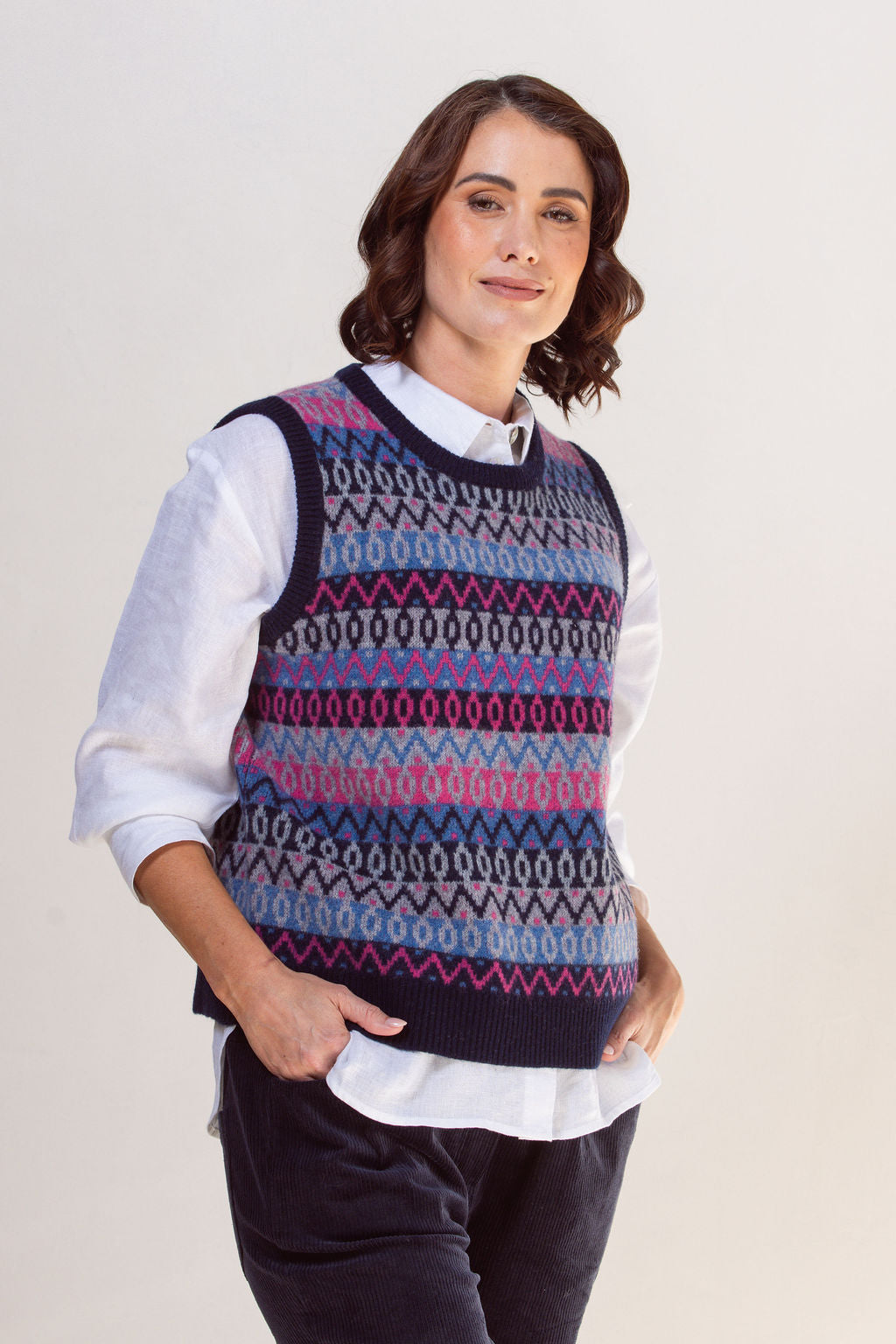 Woman wearing a See Saw jacquard patterned sweater vest over a white shirt on a plain background