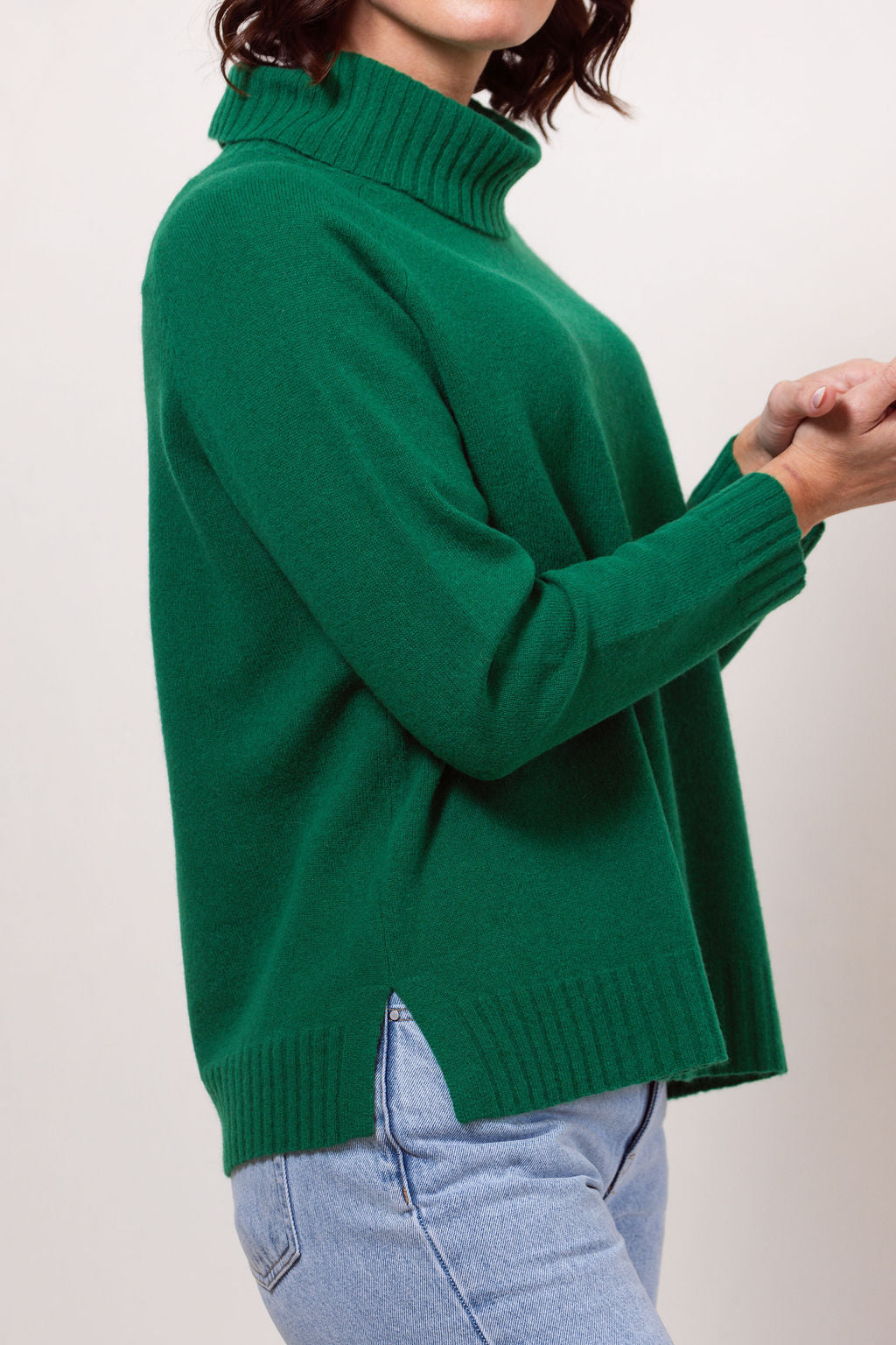 Woman wearing a green See Saw roll neck sweater against a white background