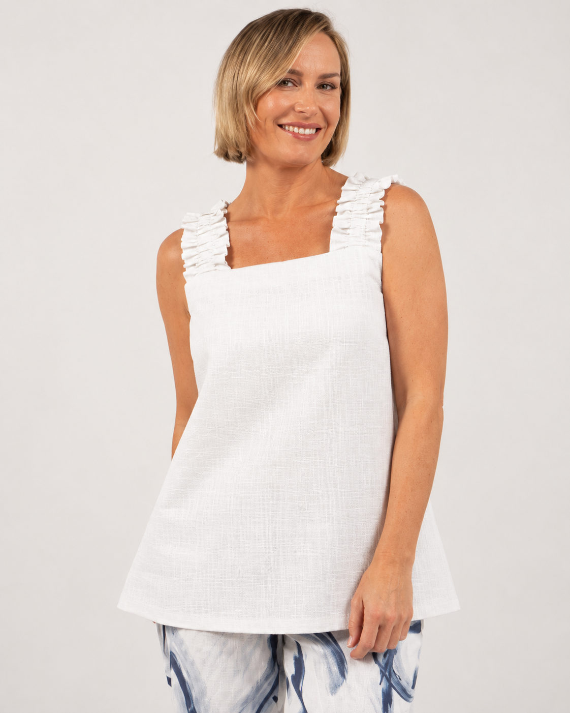 Model wears white linen see saw top with square neck. Model is standing in a neutral toned studio.