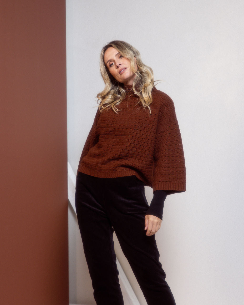 Woman wearing a See Saw copper pointelle sweater and polka dot shirt standing against a white background.