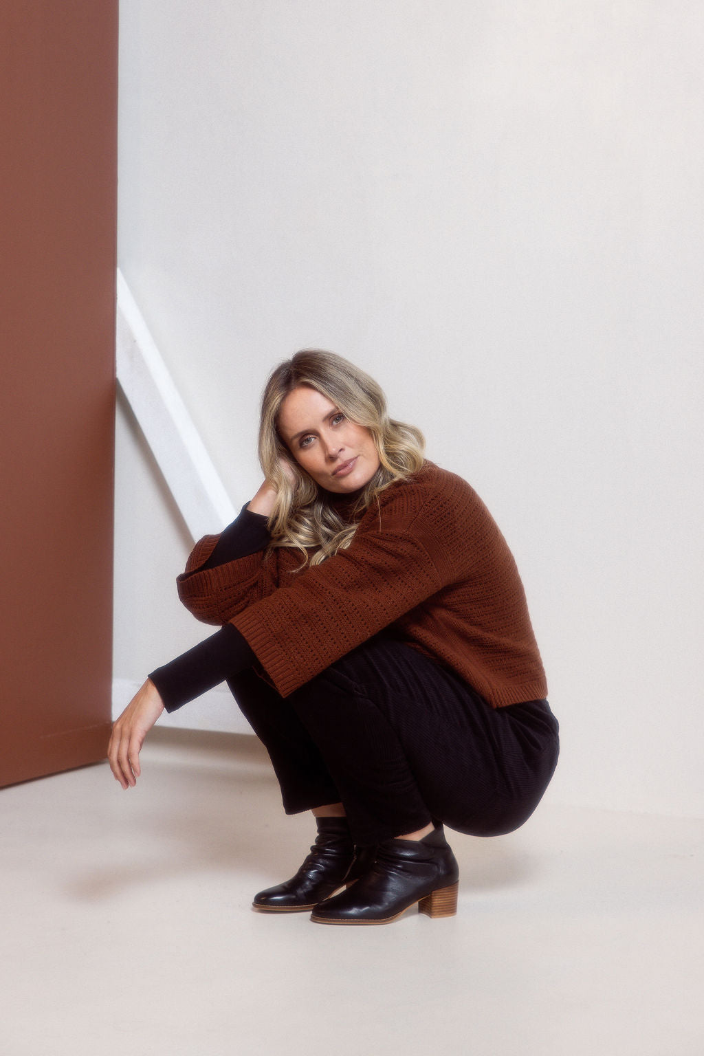Woman wearing a See Saw copper pointelle sweater and polka dot shirt standing against a white background.