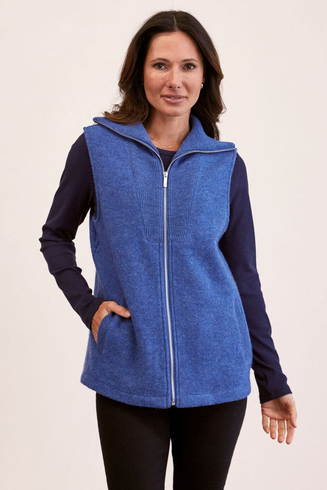 Woman wearing a Boiled wool See Saw denim vest over a dark long-sleeve shirt on a beige background