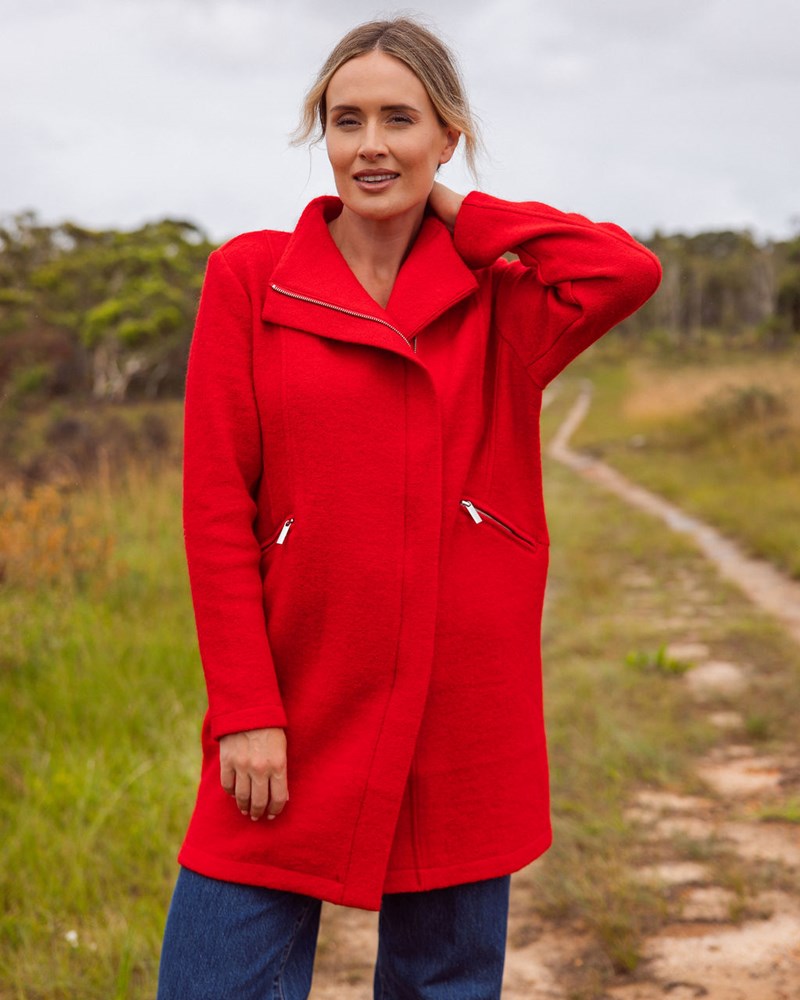 Woman wearing a See Saw boiled wool
red coat standing on a dirt path with trees in the background