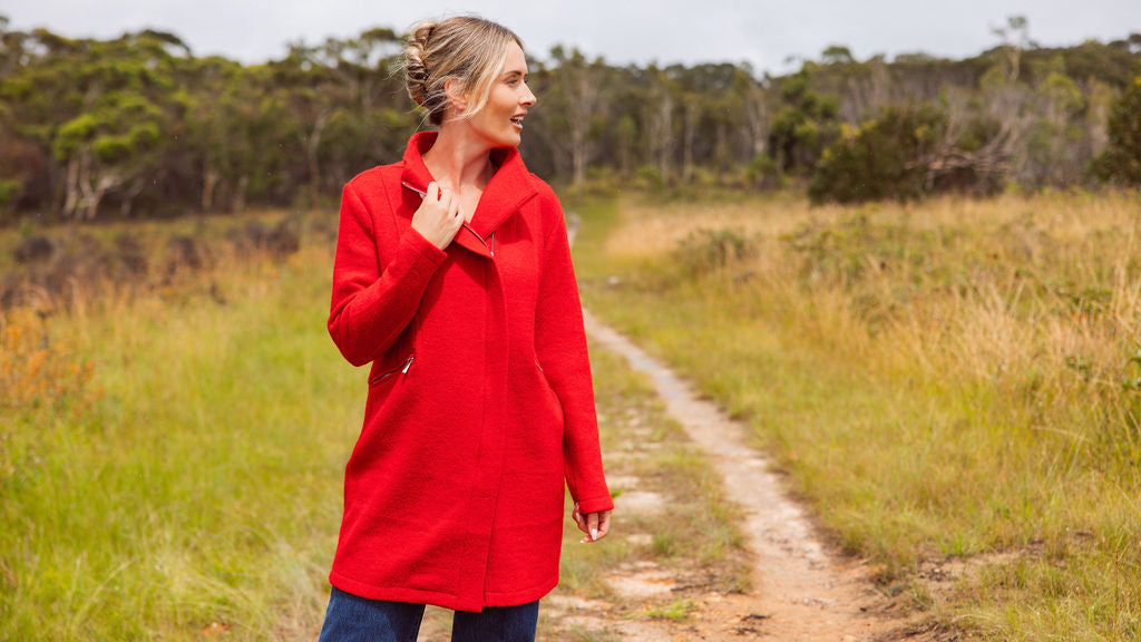 Woman wearing a See Saw boiled wool
red coat standing on a dirt path with trees in the background