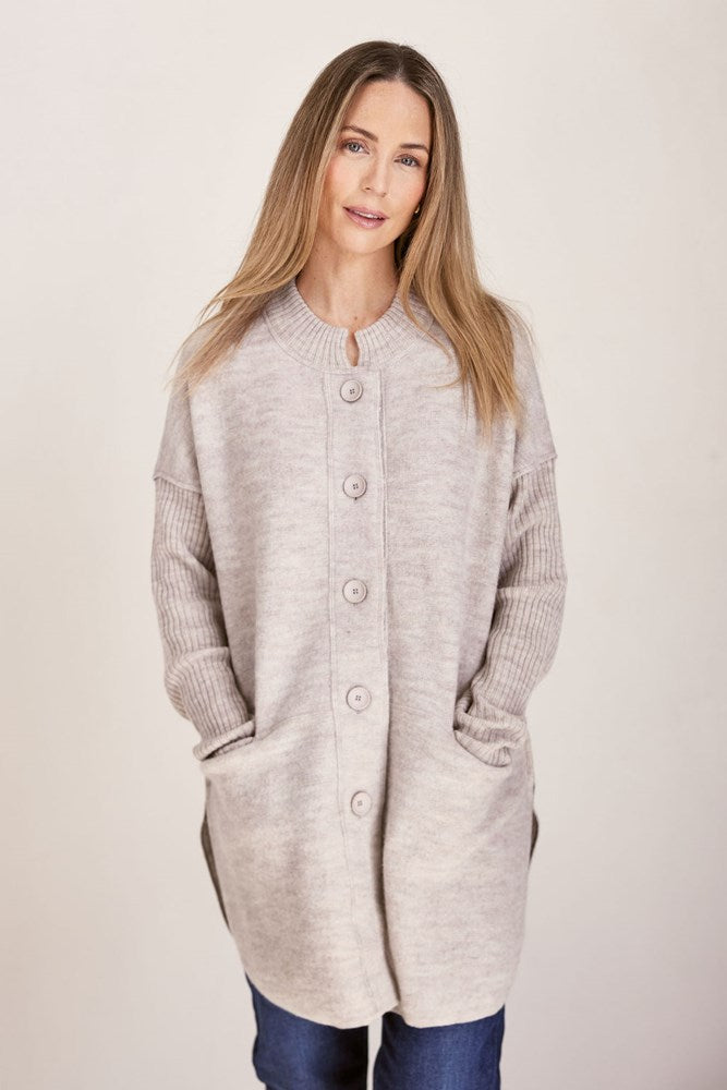 Woman wearing a long beige boiled wool See Saw cardigan on a plain background