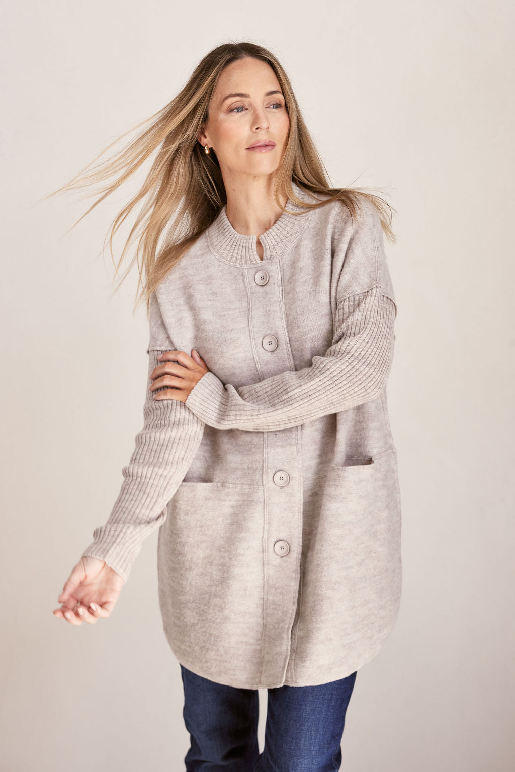 Woman wearing a long beige boiled wool See Saw cardigan on a plain background