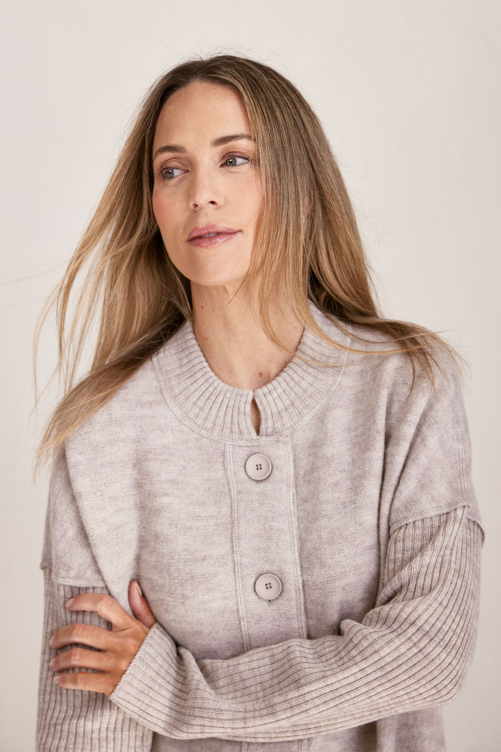 Woman wearing a long beige boiled wool See Saw cardigan on a plain background