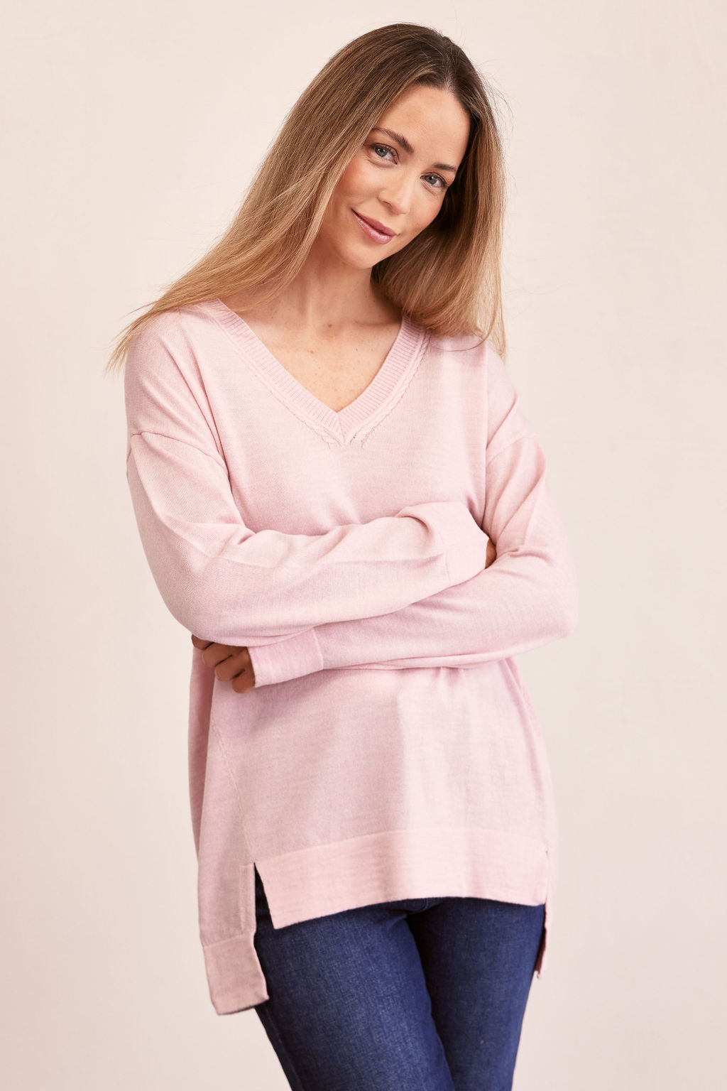 Woman wearing a light pink See Saw merino sweater and blue jeans on a beige background