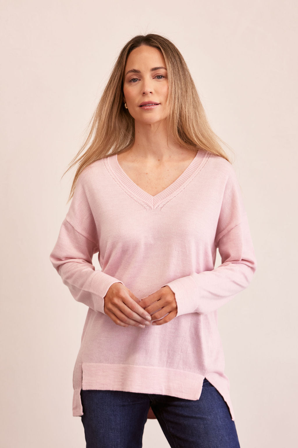 Woman wearing a light pink See Saw merino sweater and blue jeans on a beige background
