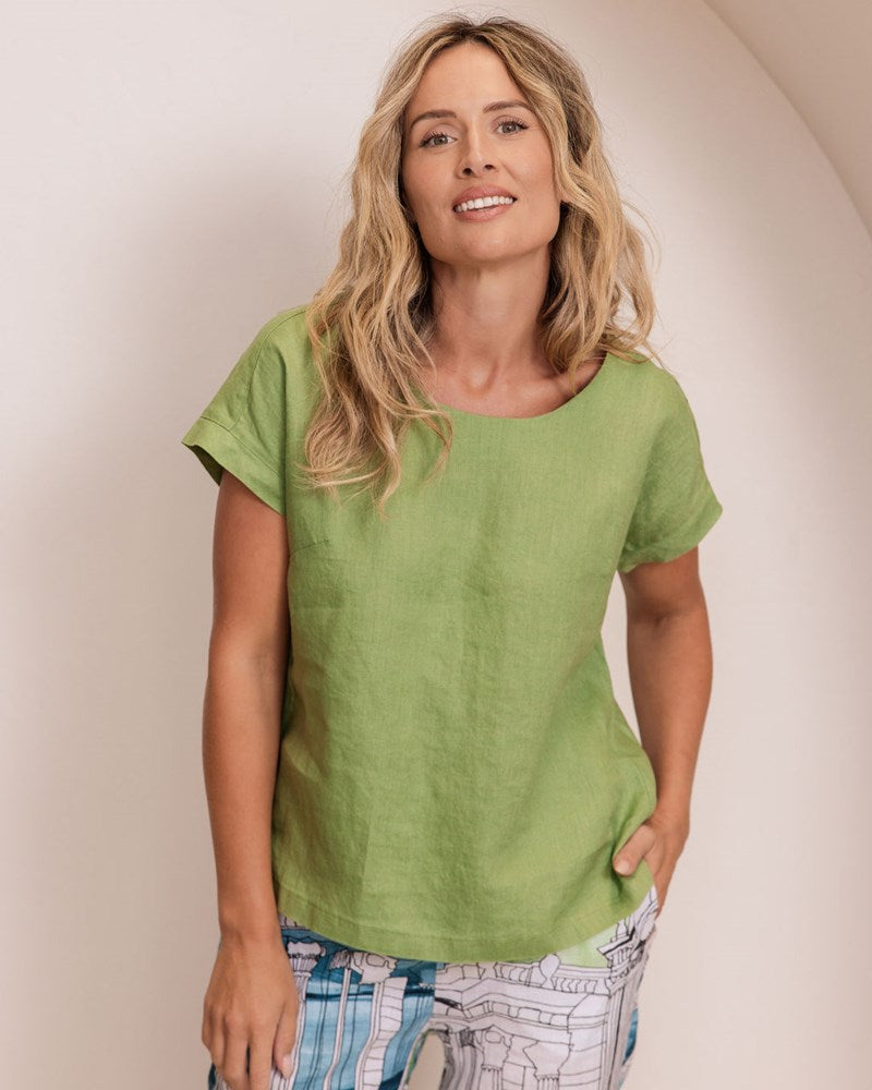 Woman in a green Linen See Saw top and patterned pants standing in a minimalistic setting.