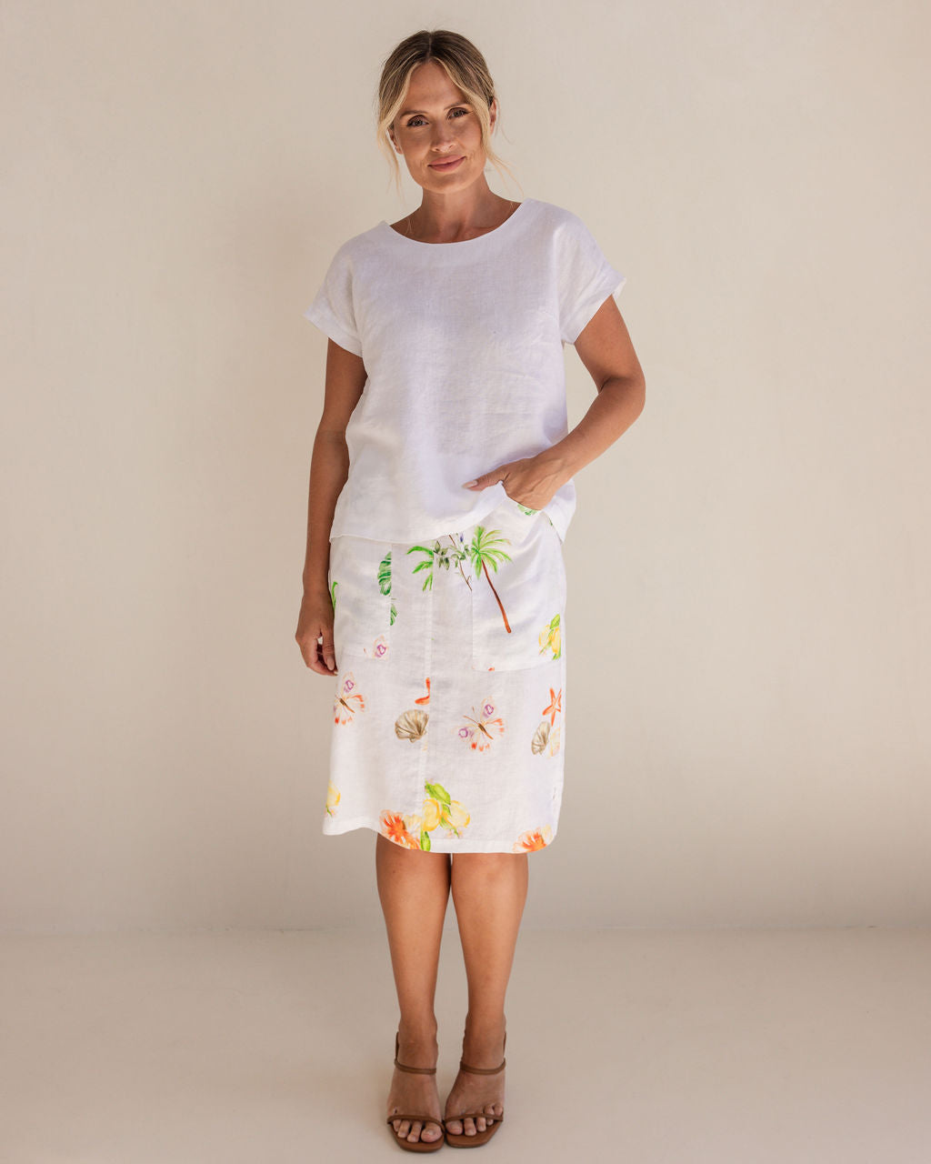 Woman in a white Linen See Saw top and pattern skirt standing in a minimalistic setting.