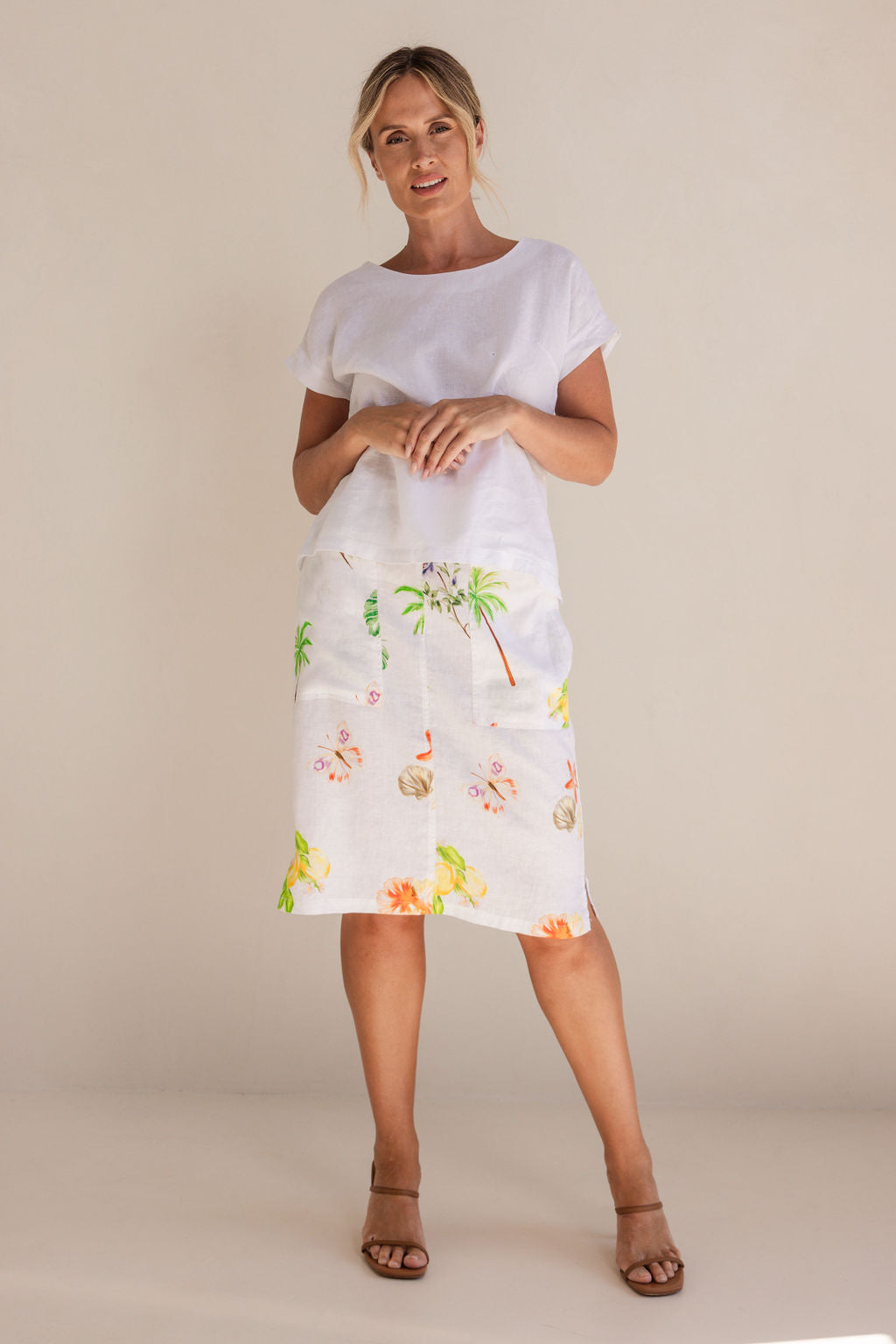Woman in a white Linen See Saw top and pattern skirt standing in a minimalistic setting.