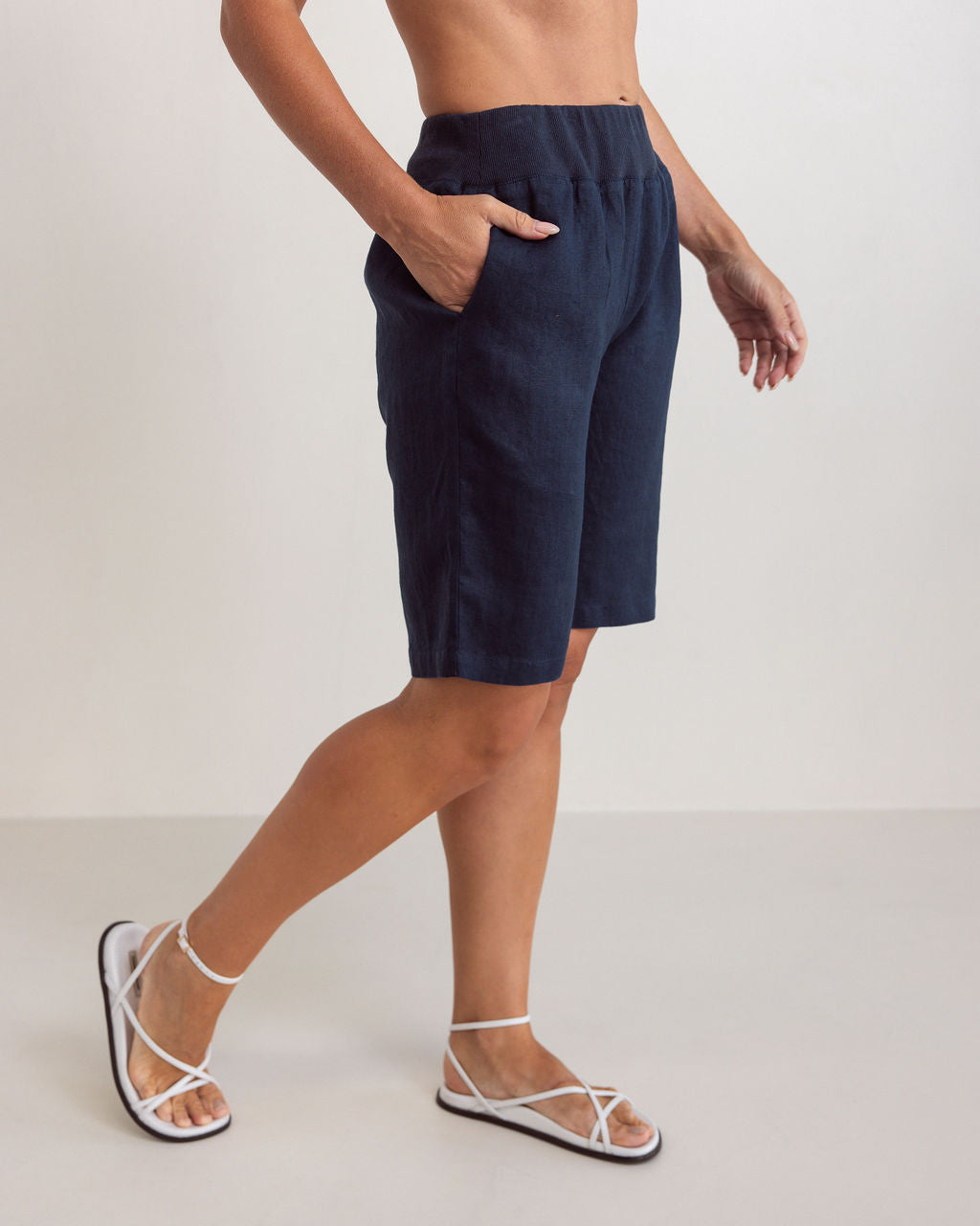 Woman wearing knee length navy linen See Saw shorts with an elastic waist against a white background. 