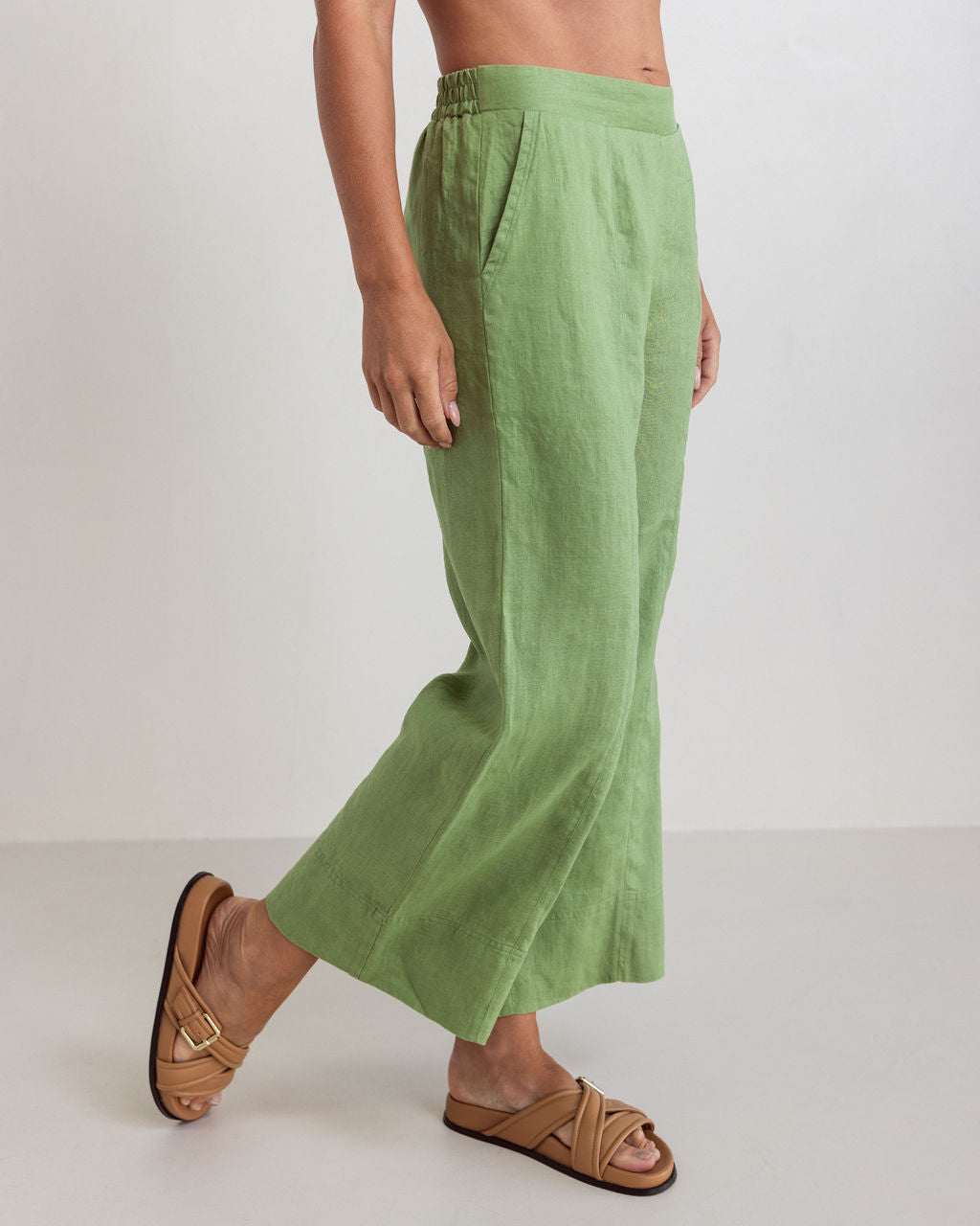 Woman wearing See Saw linen wide leg pants in pistachio with brown sandals against a white background