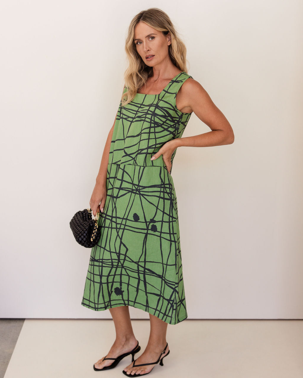Woman wearing a green linen See Saw patterned dress against a white background