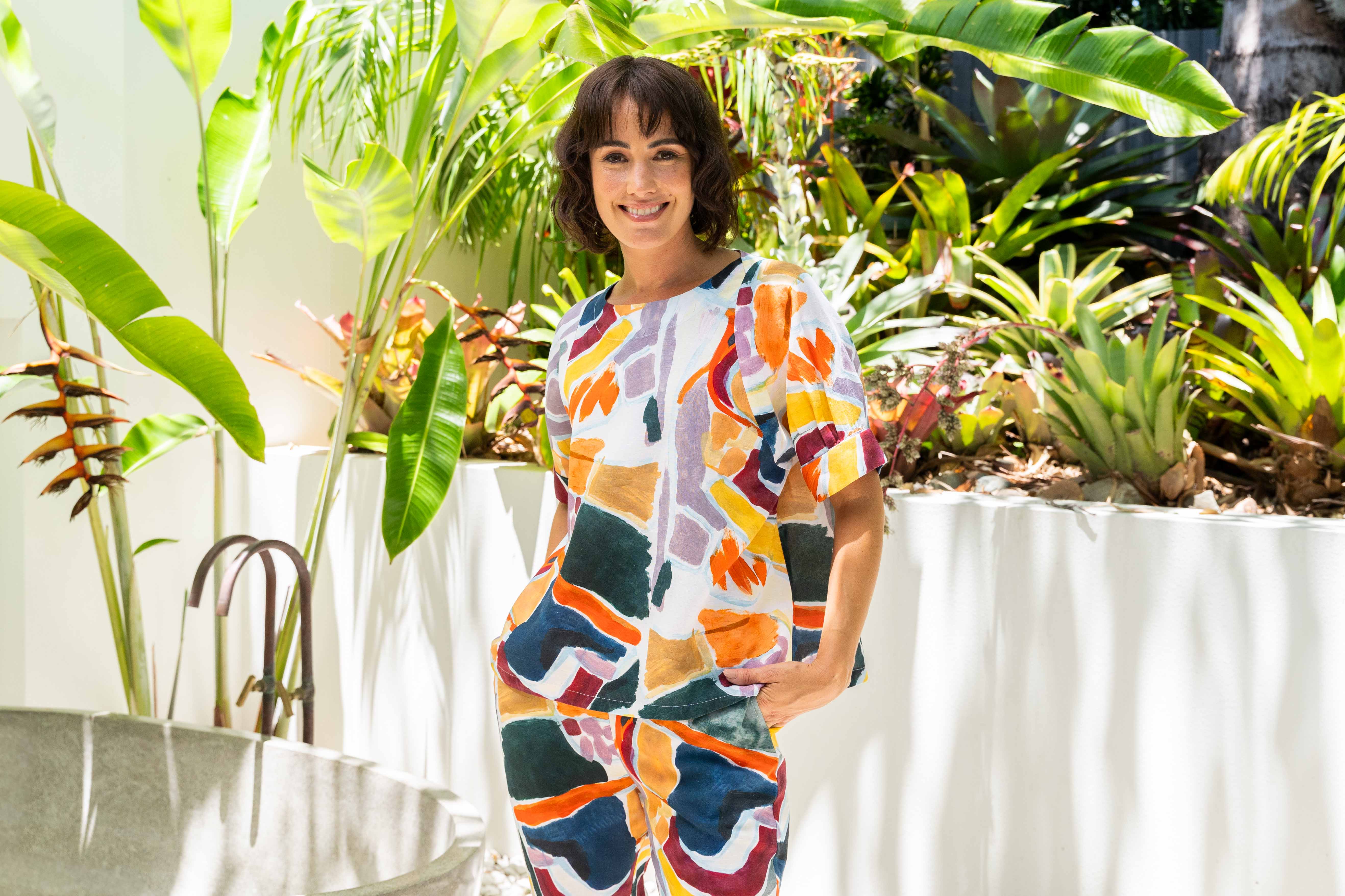 Woman in a colorful See Saw Linen pant set standing in a garden with plants and a chair.