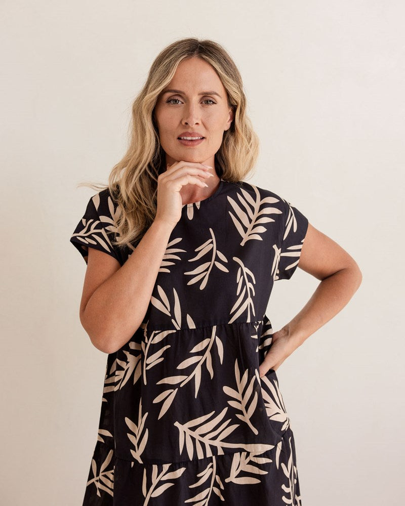 Woman wearing a black dress with beige leaf pattern against a plain background. See Saw Cotton Tiered Dress