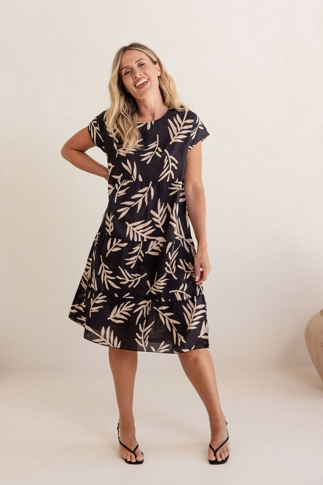 Woman wearing a black dress with beige leaf pattern on a white background. See Saw Cotton Tiered Dress