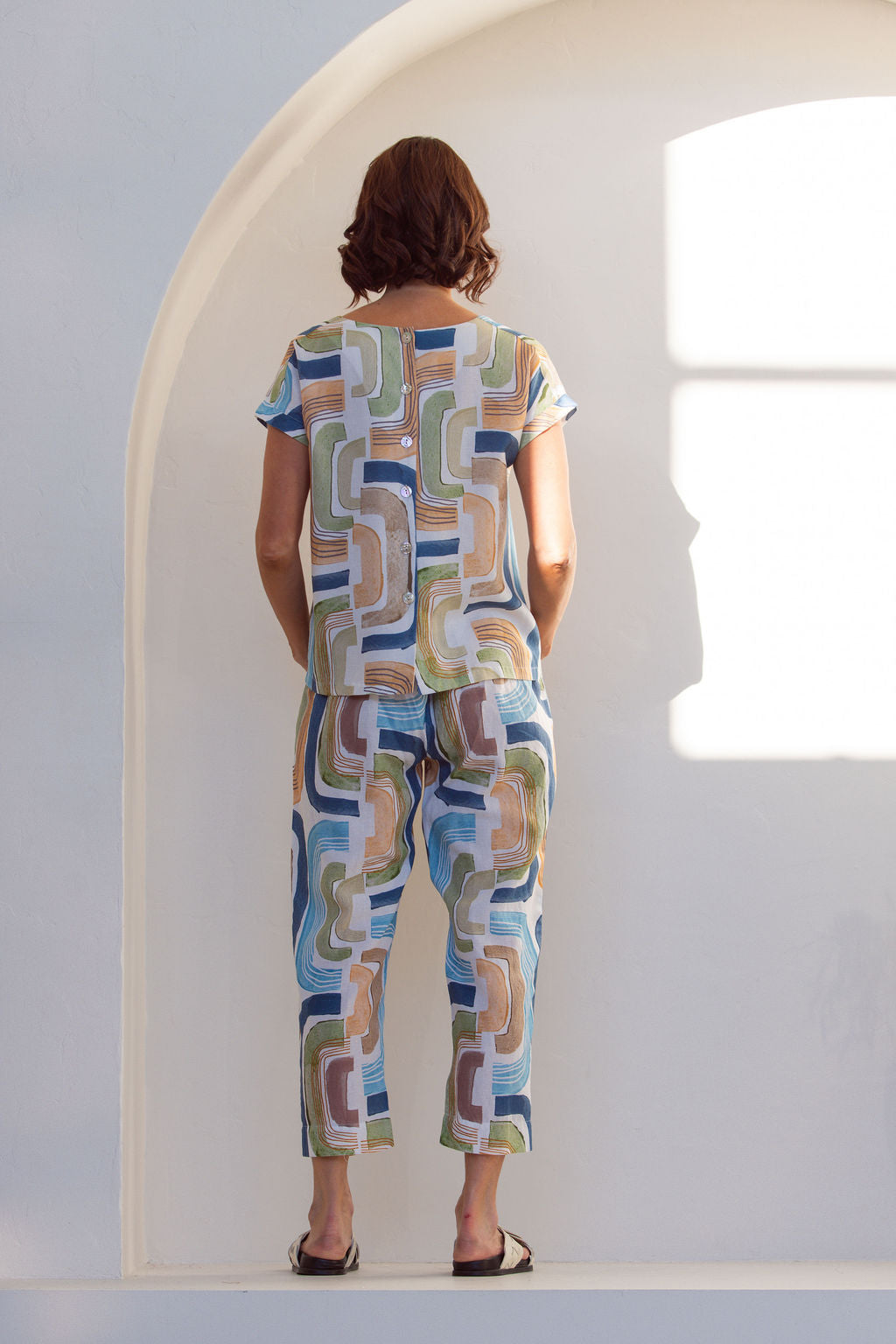 Woman wearing abstract  See Saw seascape outfit standing in a bright, sunlit room with white walls and a plant.