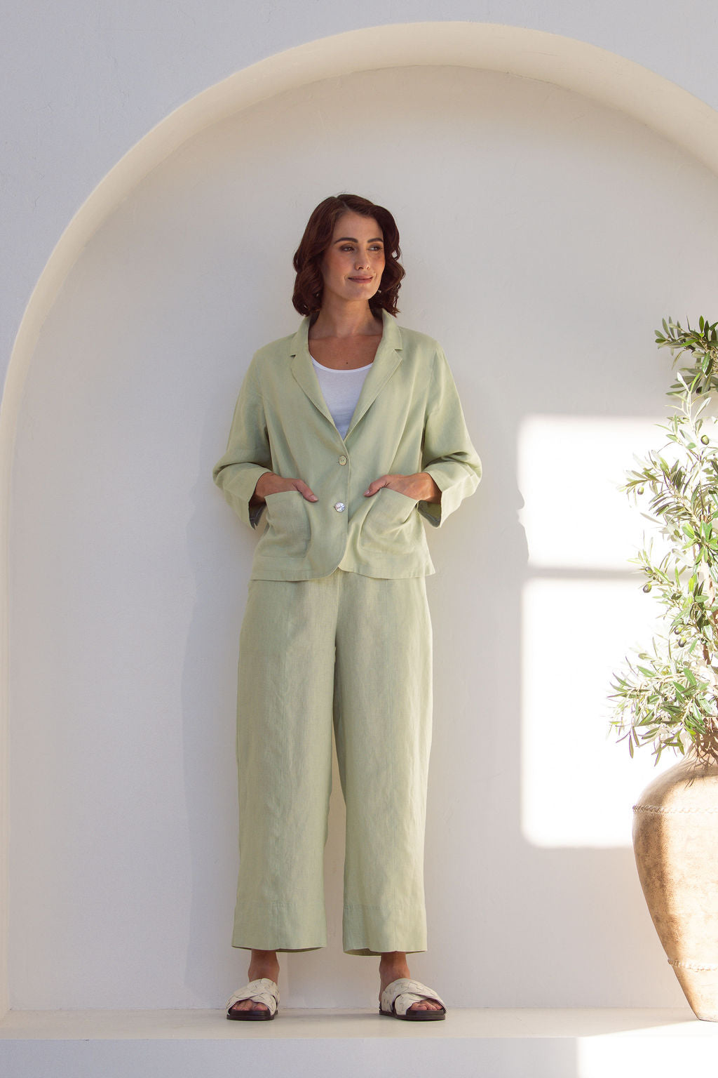 Woman in a light green Linen See Saw outfit standing in a minimalistic room with a plant.