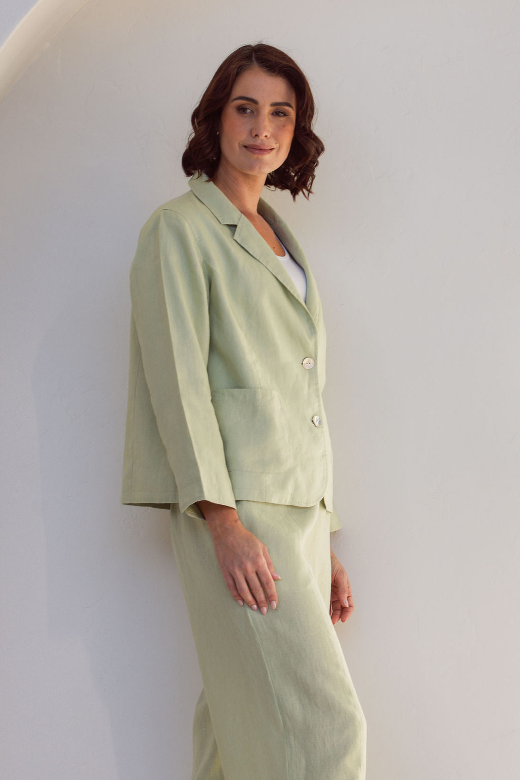 Woman in a light green Linen See Saw outfit standing in a minimalistic room with a plant.