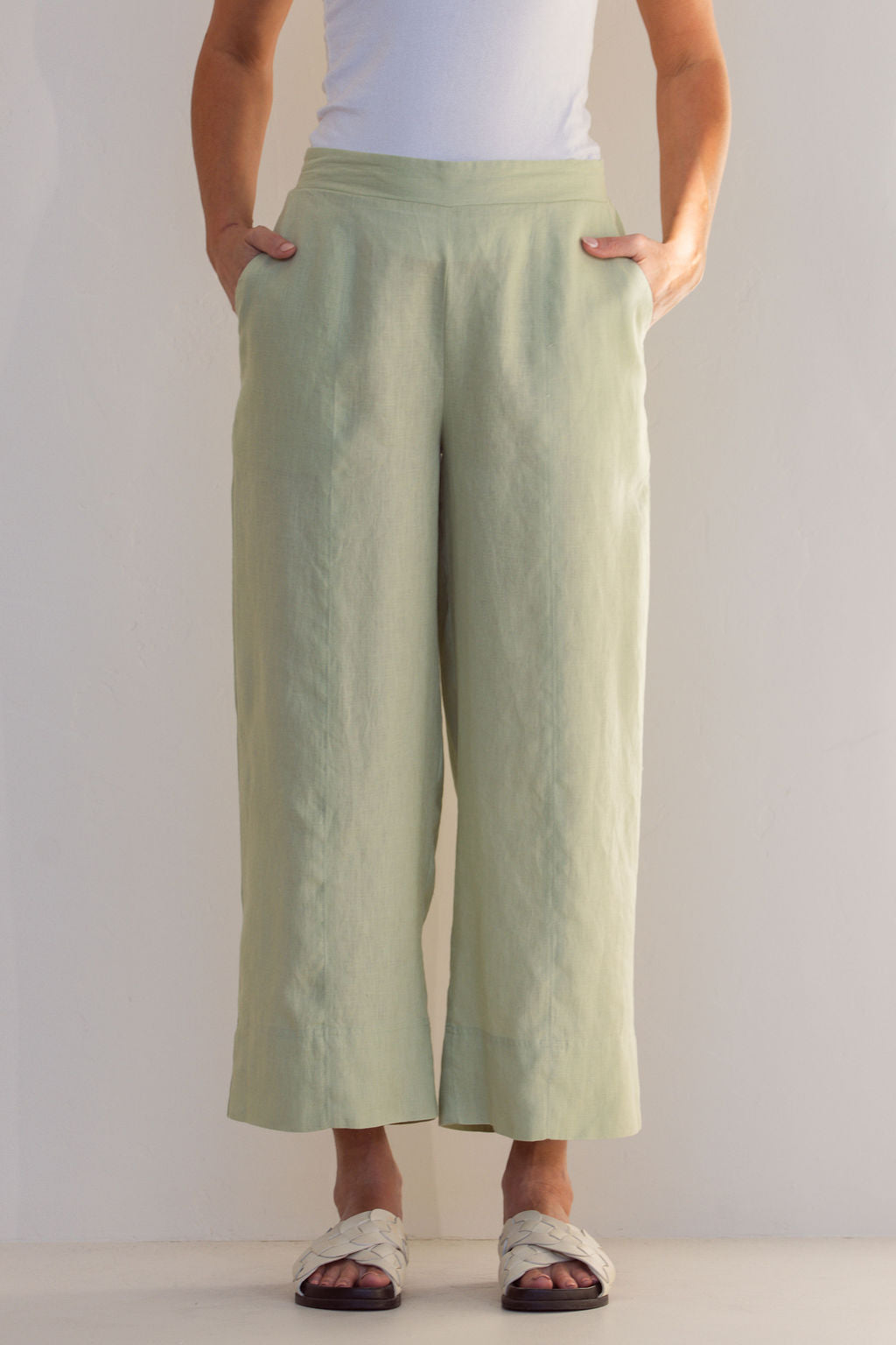 Woman in a light green Linen See Saw outfit standing in a minimalistic room with a plant.