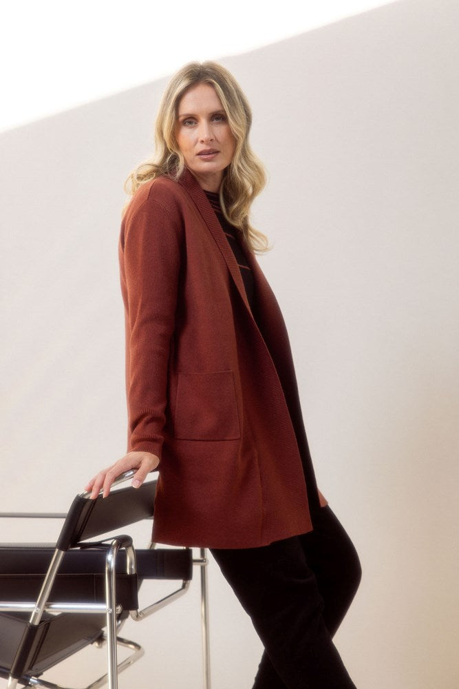 Woman wearing a brown See Saw cardigan standing next to a chair against a white background