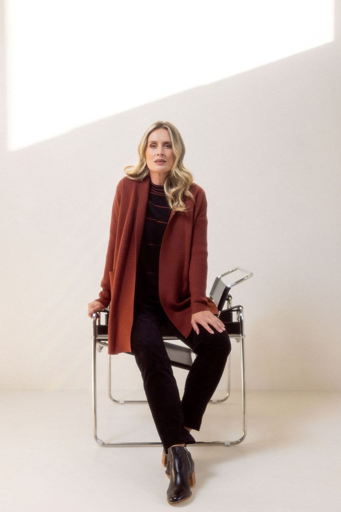 Woman wearing a brown See Saw cardigan standing next to a chair against a white background