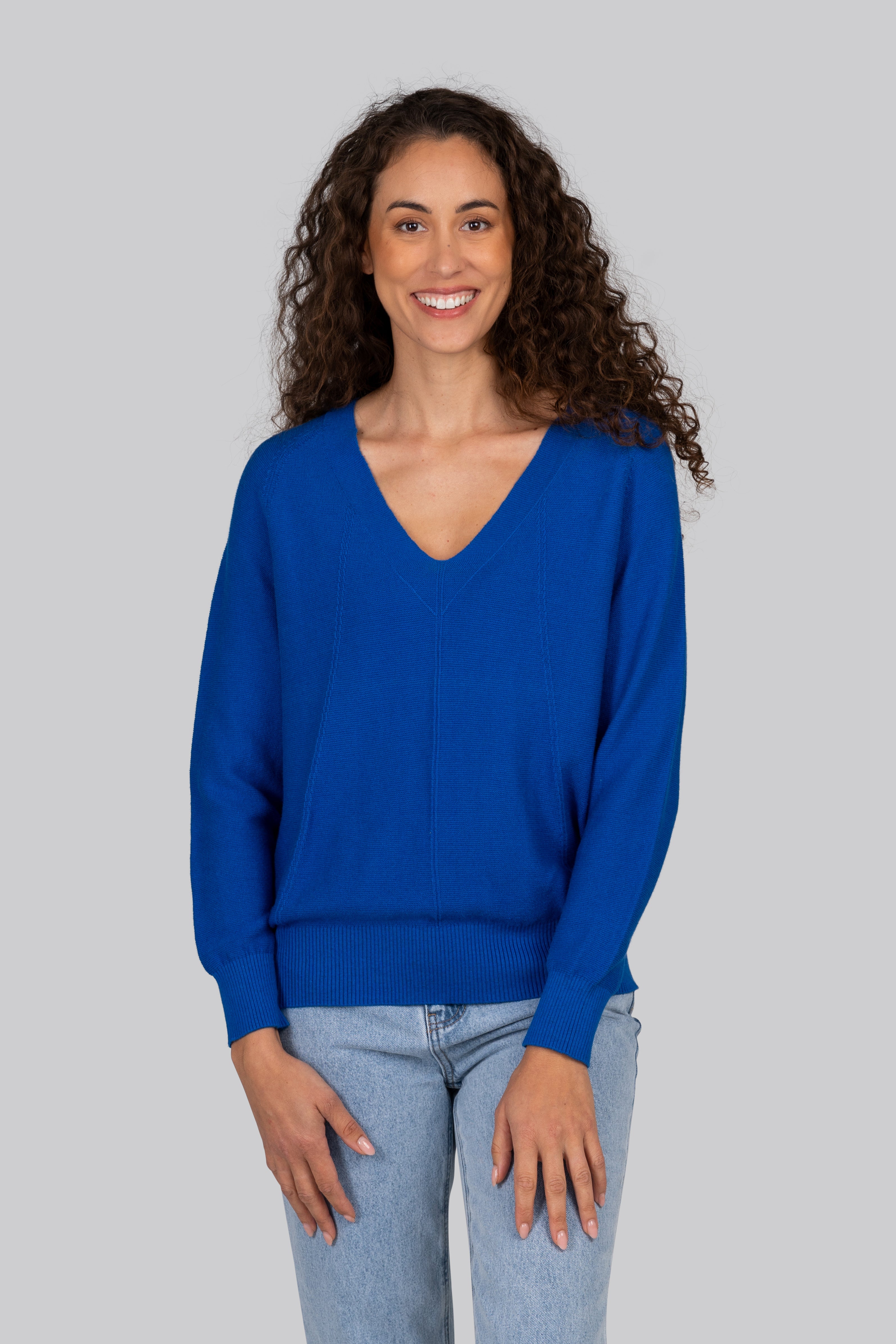 Woman wearing a blue Kaleido textured sweater and colorful pants standing by a marina with boats in the background.