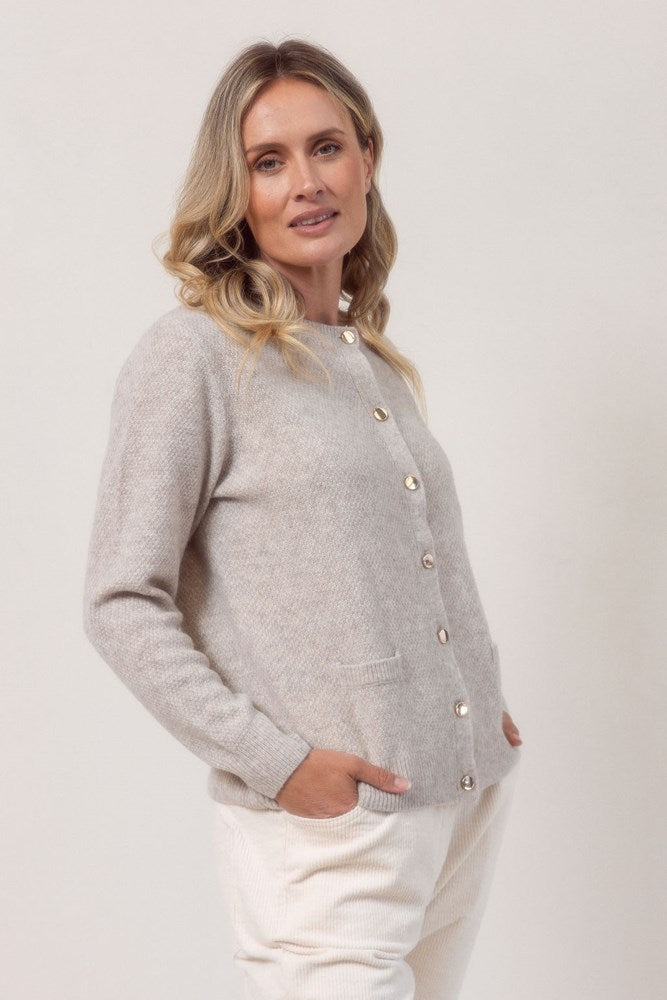 Woman wearing a wheat colour See Saw cardigan in wool and yak with buttons on a white background