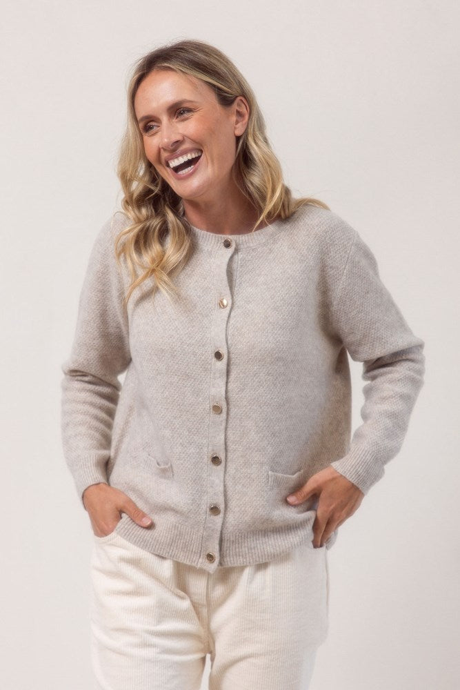 Woman wearing a wheat colour See Saw cardigan in wool and yak with buttons on a white background