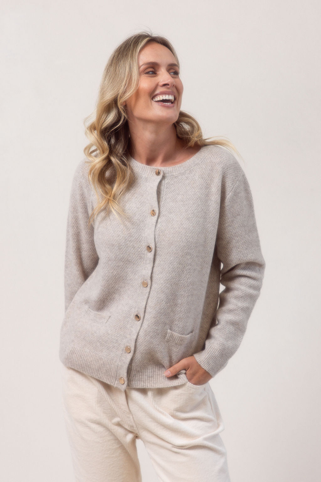 Woman wearing a wheat colour See Saw cardigan in wool and yak with buttons on a white background