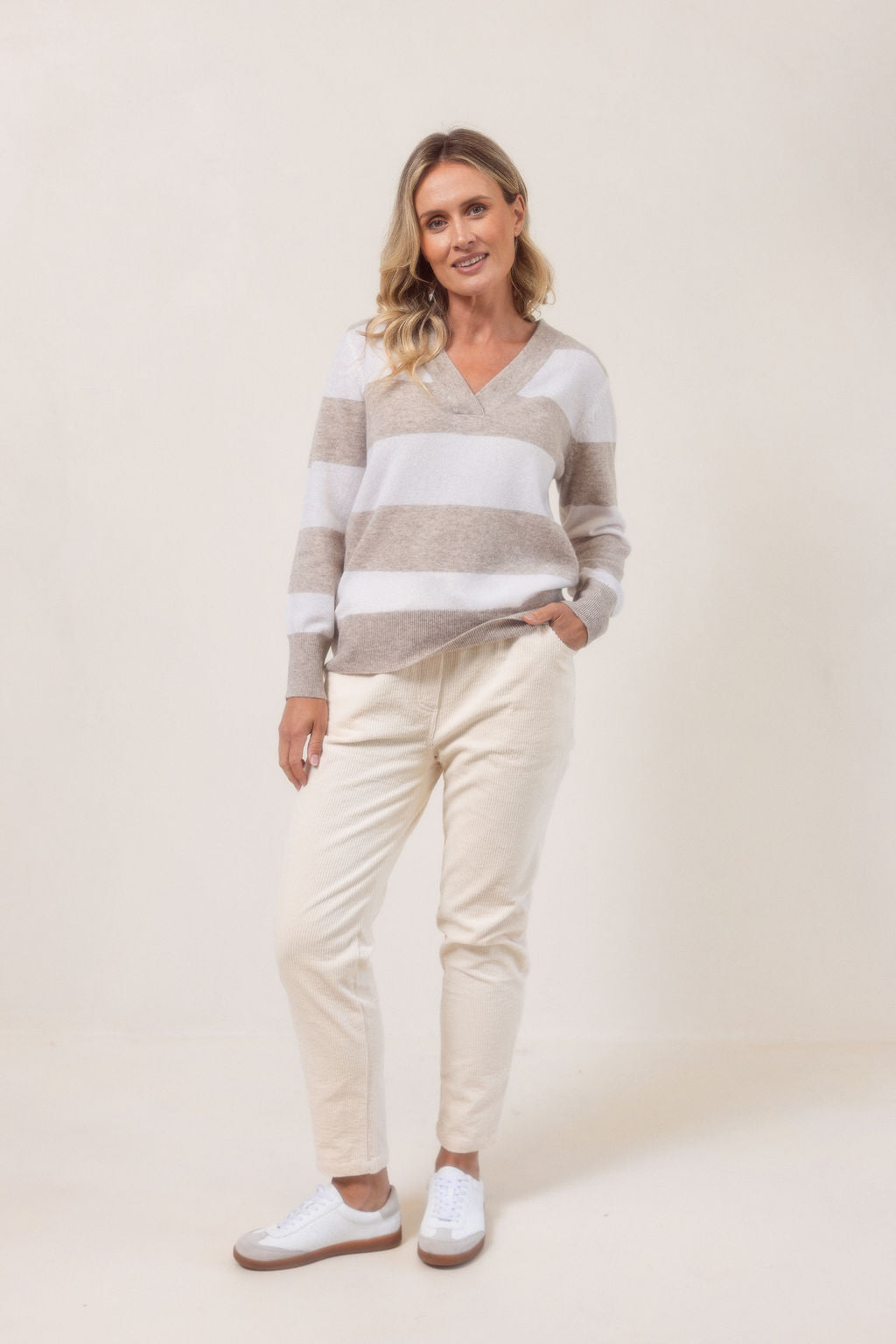 Woman wearing a striped Merino Wool See Saw sweater and beige pants against a plain background