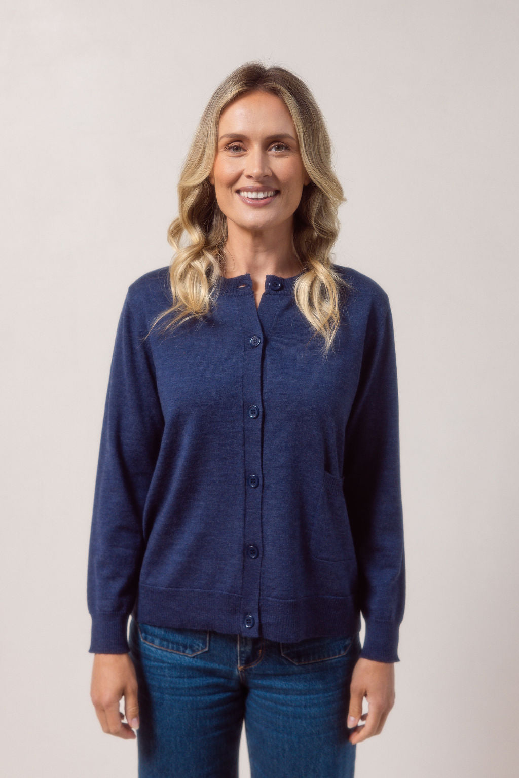 Woman wearing a merino wool See Saw indigo cardigan and blue jeans against a plain background