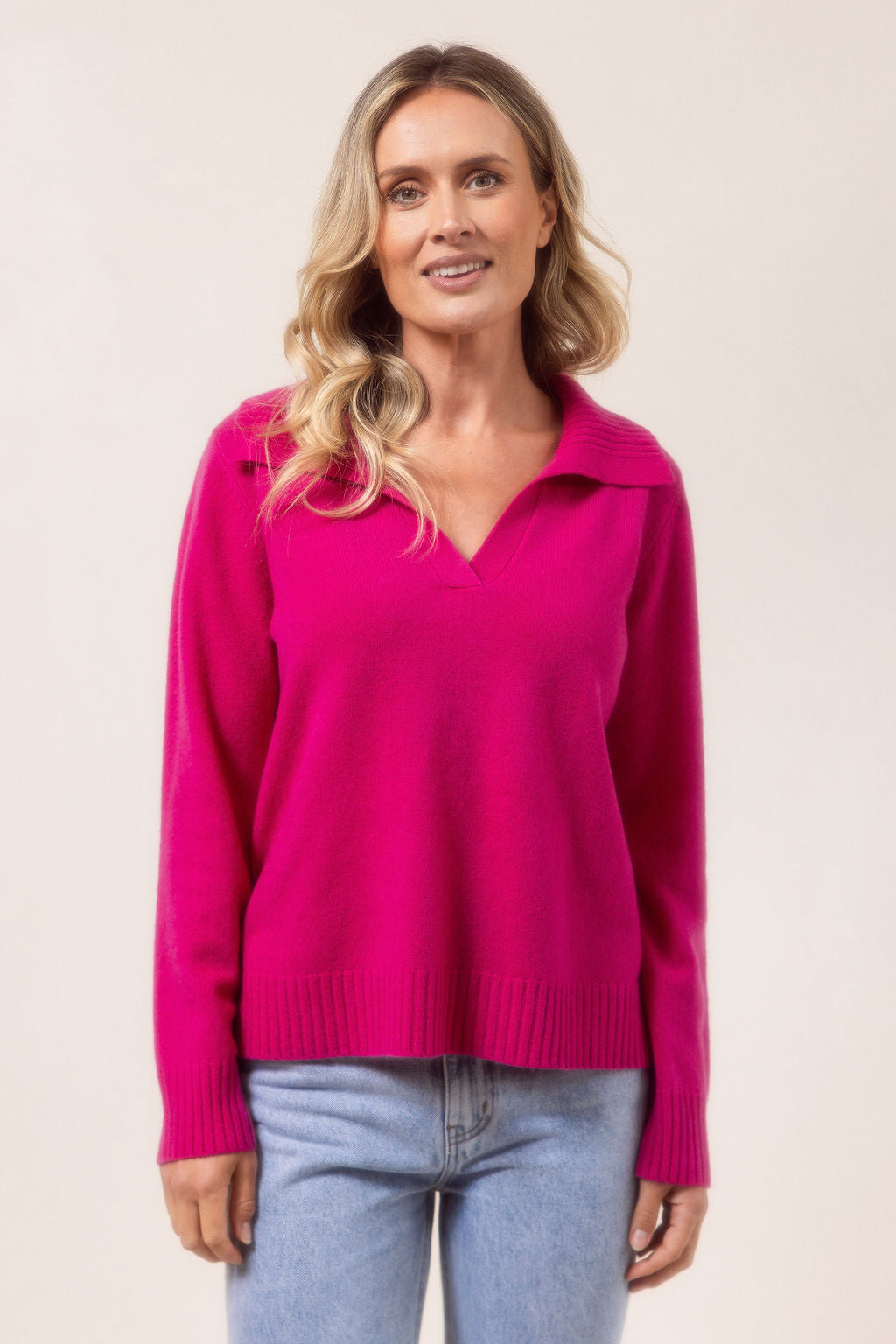 Woman wearing a bright pink See Saw sweater with a collar and light blue jeans against a plain background
