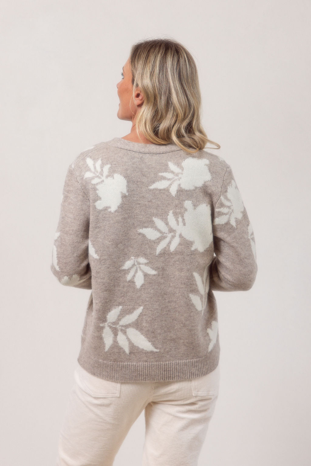 Woman wearing a oat See Saw cardigan with white floral patterns against a plain background