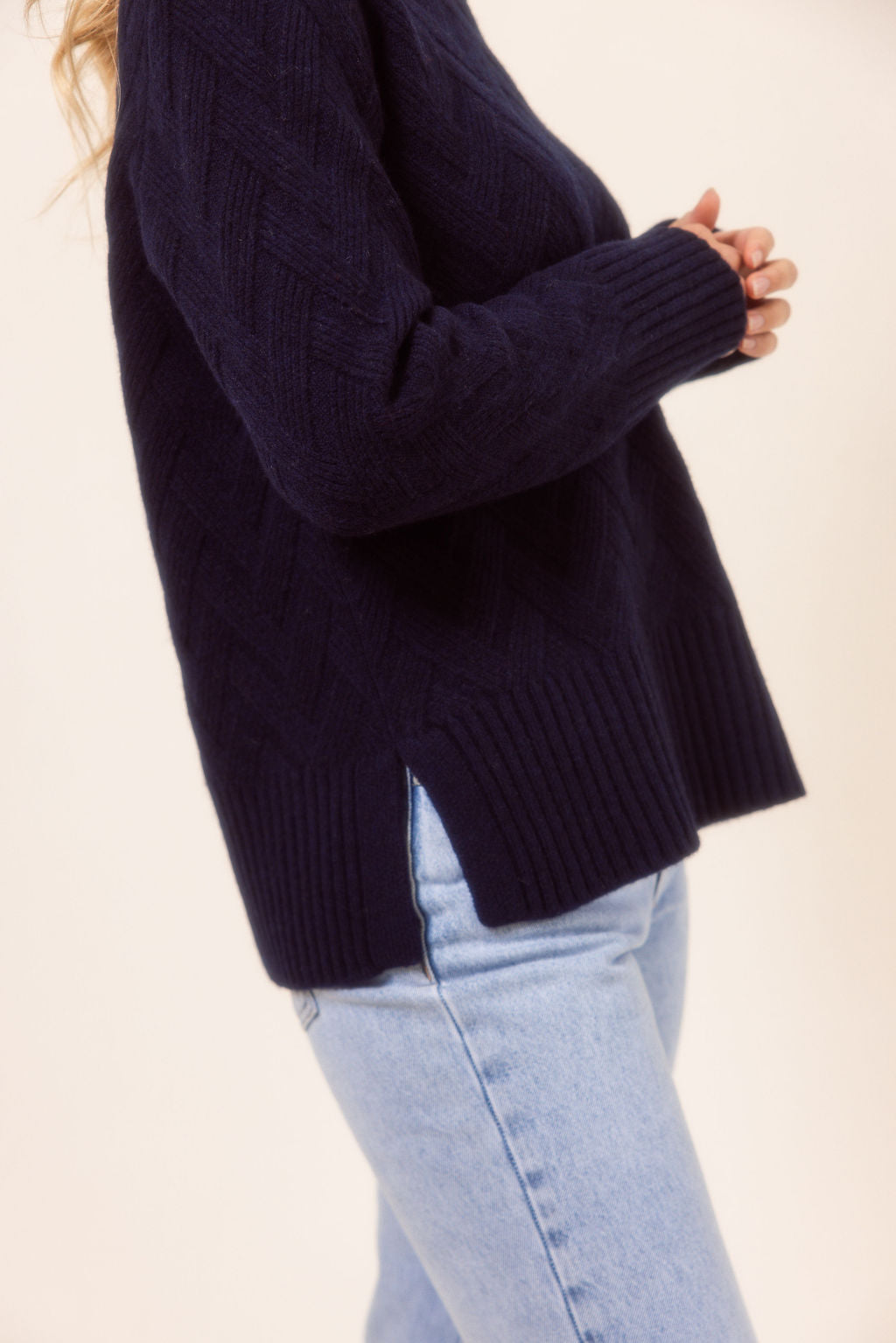 Person wearing a dark blue See saw sweater and light blue jeans on a plain background