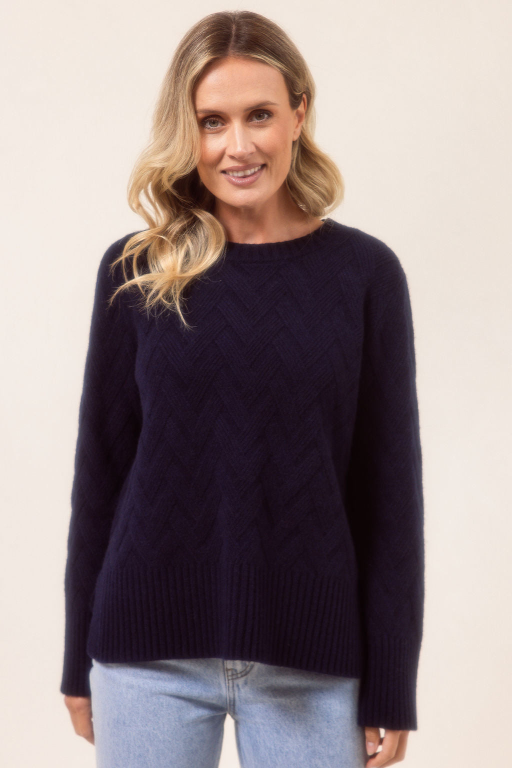 Woman wearing a navy See Saw sweater and light blue jeans on a beige background