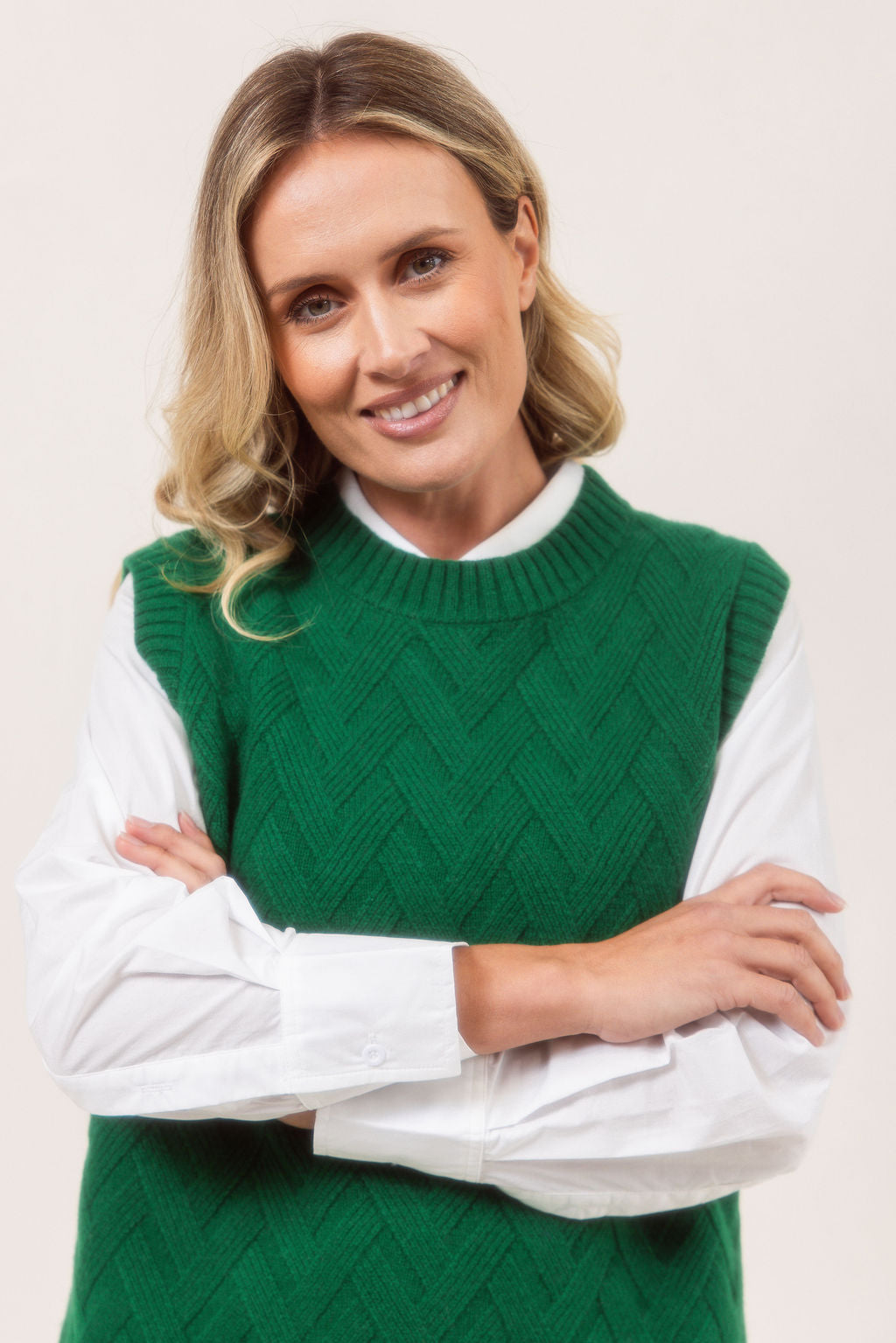 Woman wearing a See Saw green Merino Wool knitted vest over a white shirt on a plain background