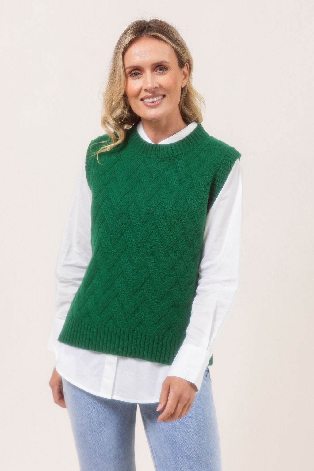 Woman wearing a See Saw green Merino Wool knitted vest over a white shirt on a plain background