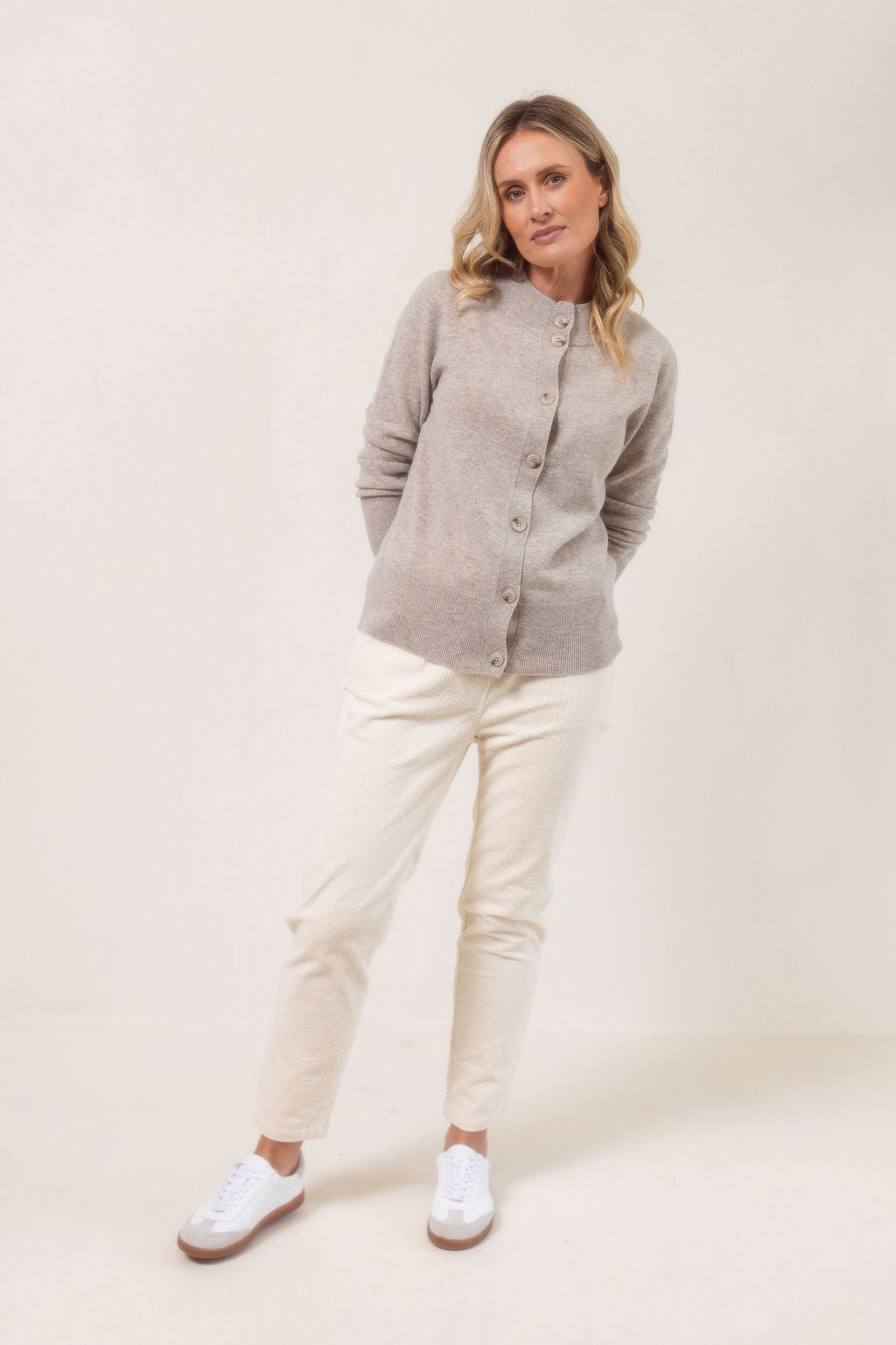 Woman wearing a wheat See Saw merino wool cardigan and light blue jeans against a plain background