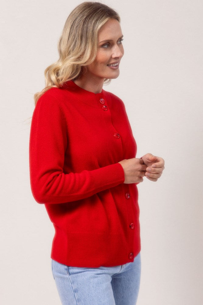 Woman wearing a red See Saw merino wool cardigan and light blue jeans against a plain background
