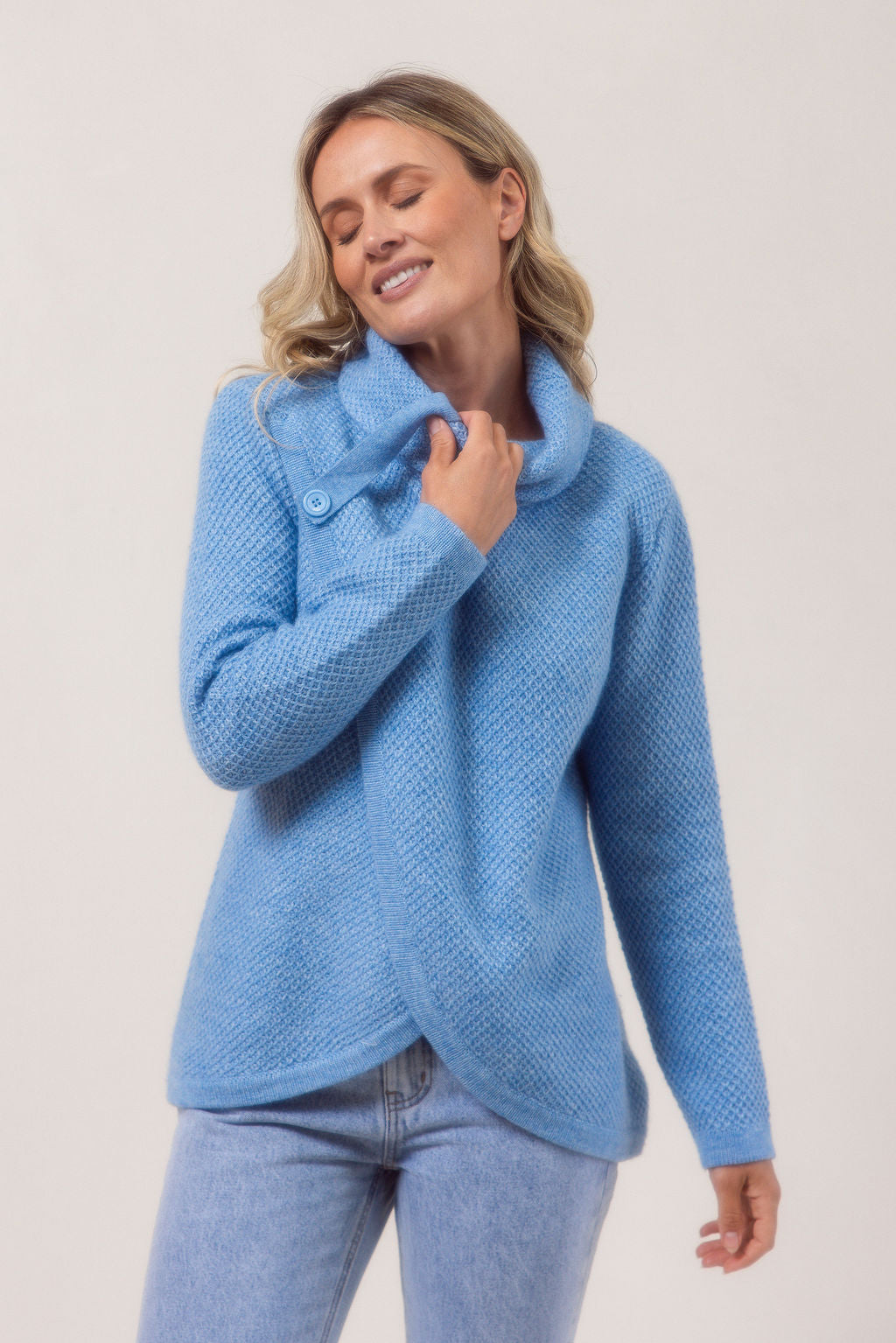 Woman wearing a powder blue Cowl Neck Moss Stitch See Saw sweater with a white background