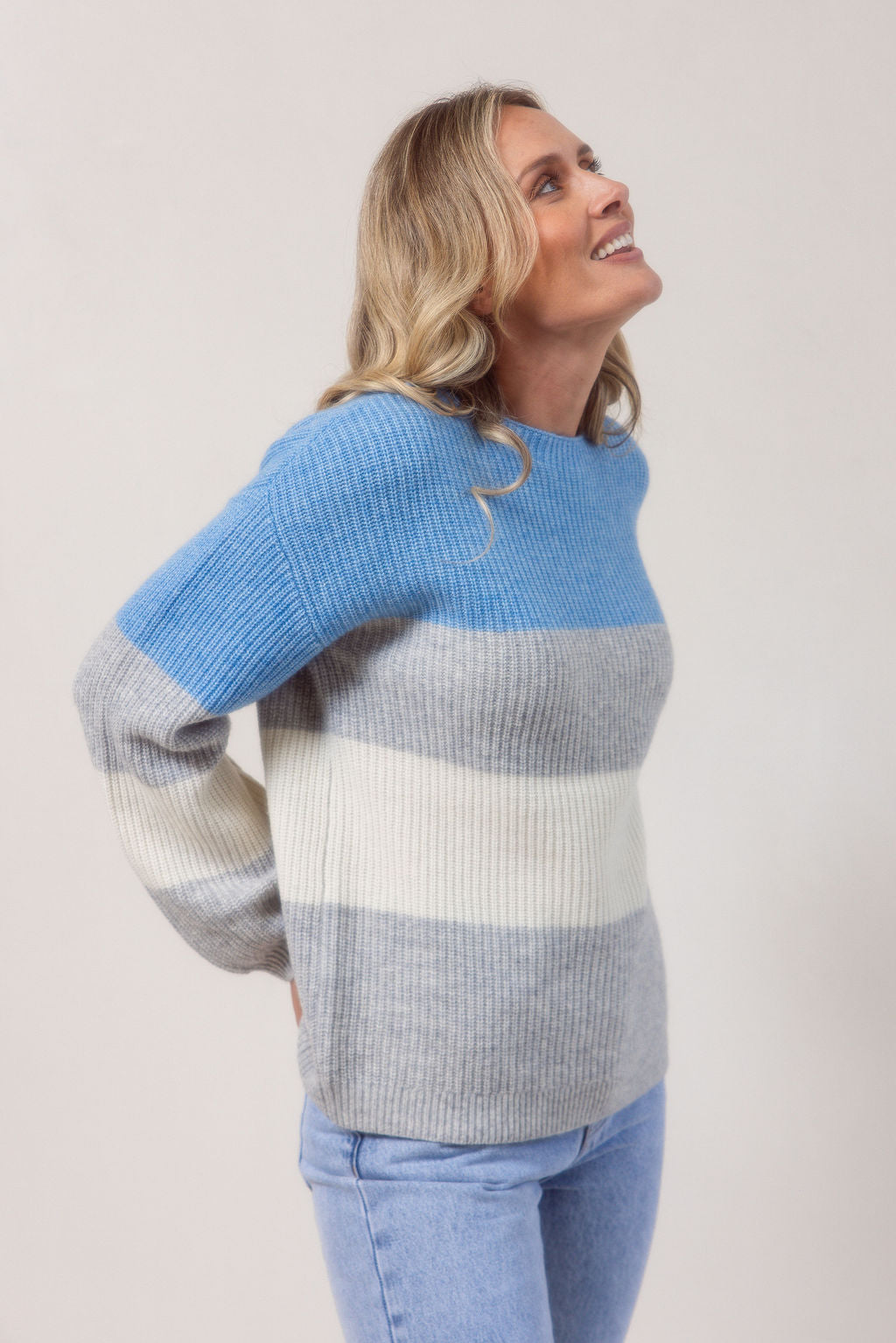 Woman wearing a blue, gray, and white striped See Saw sweater against a plain background
