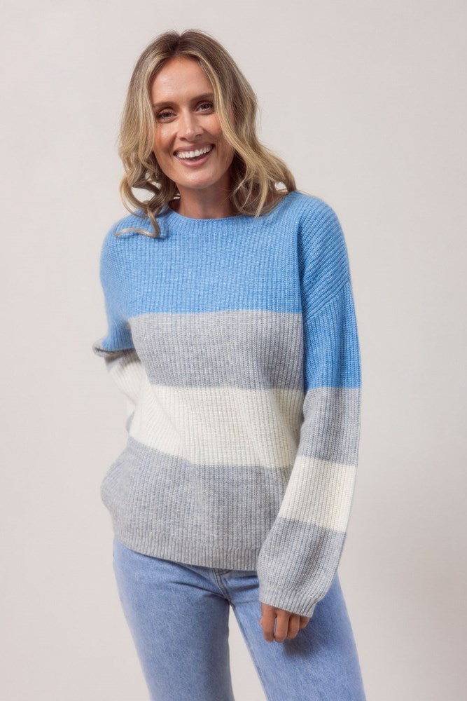 Woman wearing a blue, gray, and white striped See Saw sweater against a plain background