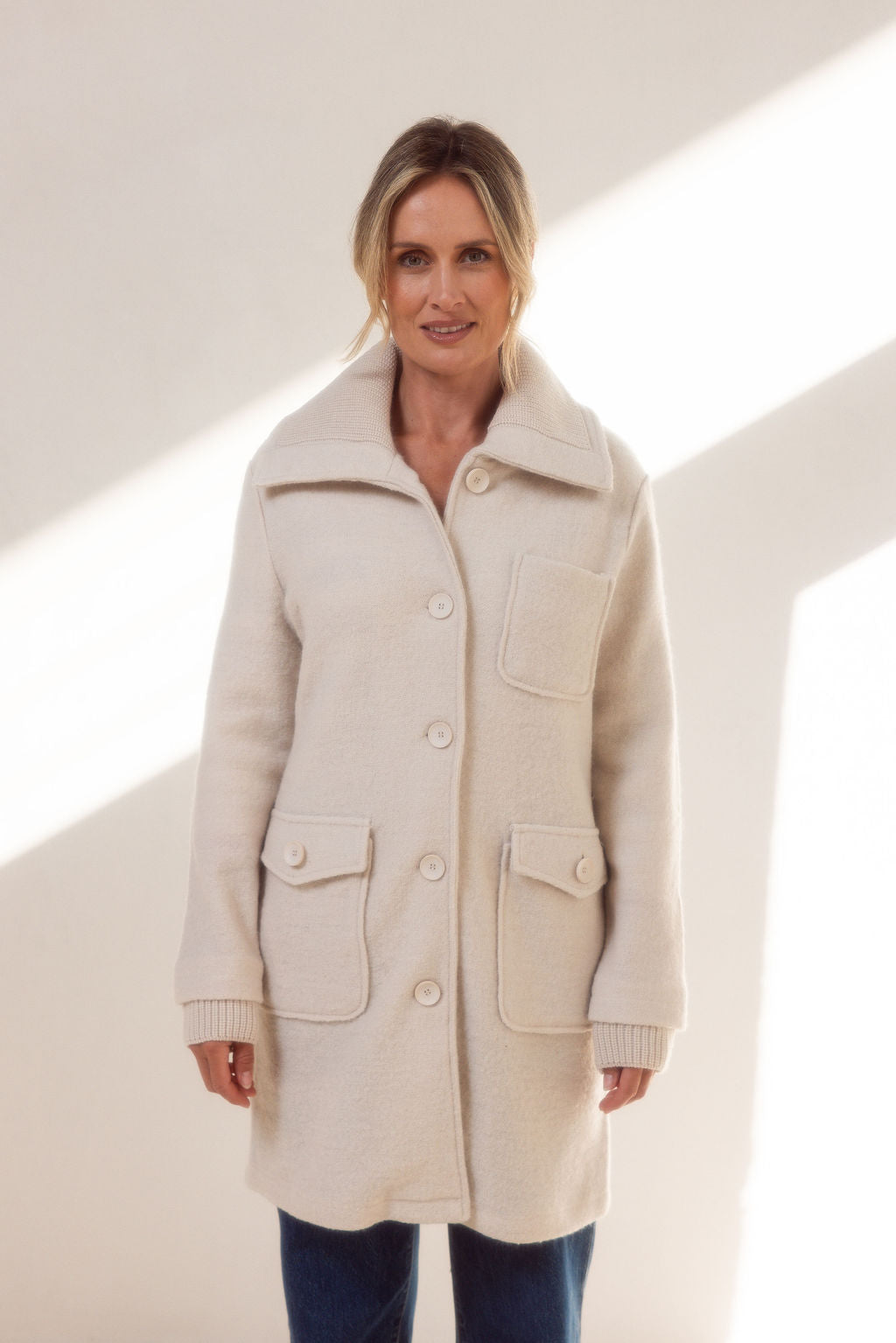 Woman wearing a beige See Saw boiled wool coat and sweater against a light background