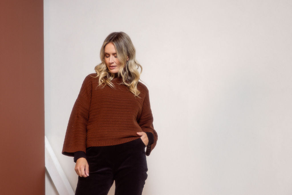 Woman wearing a See Saw copper pointelle sweater and polka dot shirt standing against a white background.