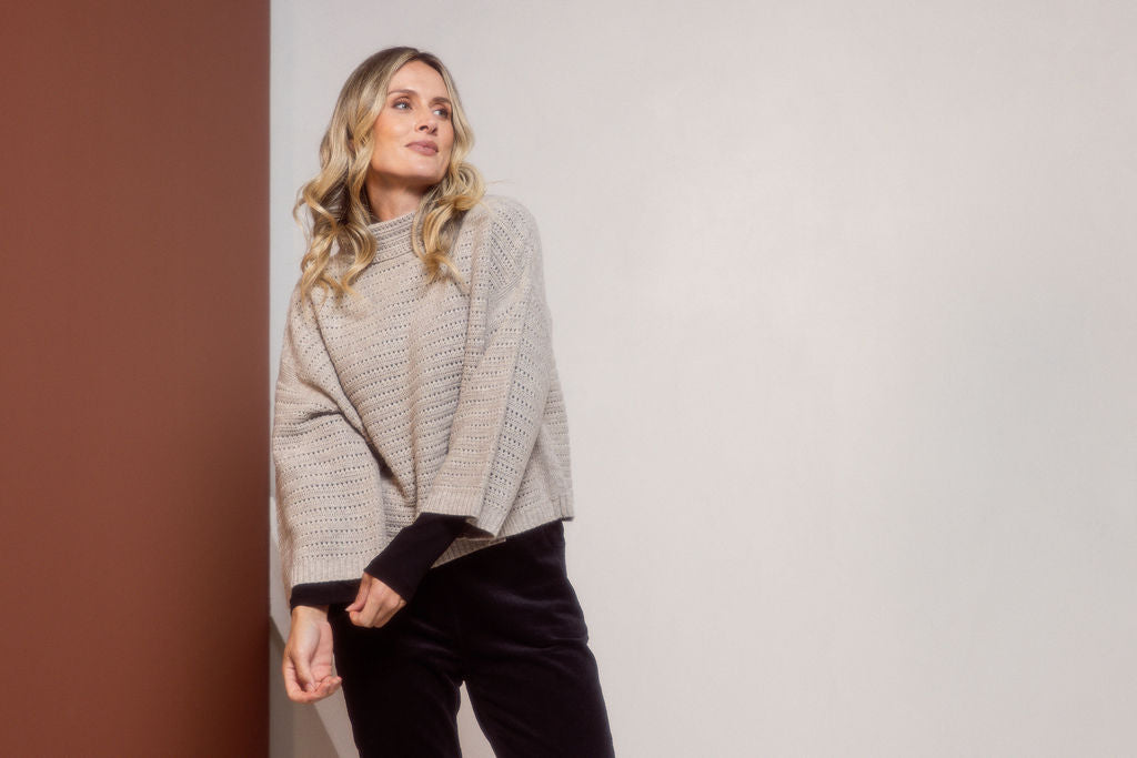 Woman wearing a See Saw Oat Marle pointelle sweater and polka dot shirt standing against a white background.