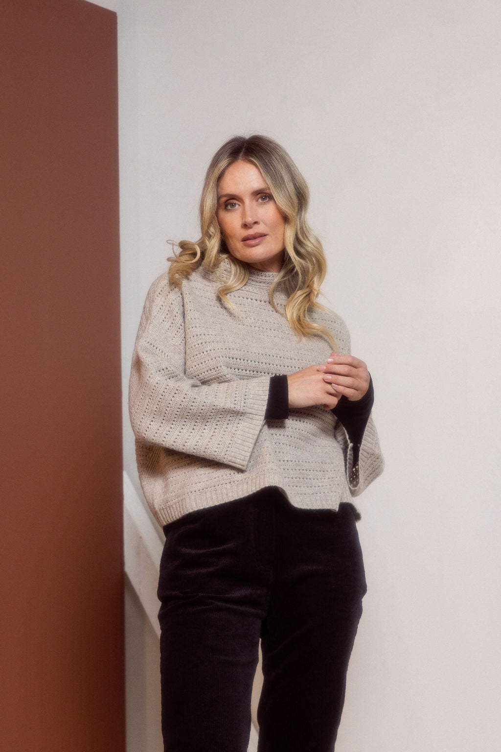 Woman wearing a See Saw Oat Marle pointelle sweater and polka dot shirt standing against a white background.