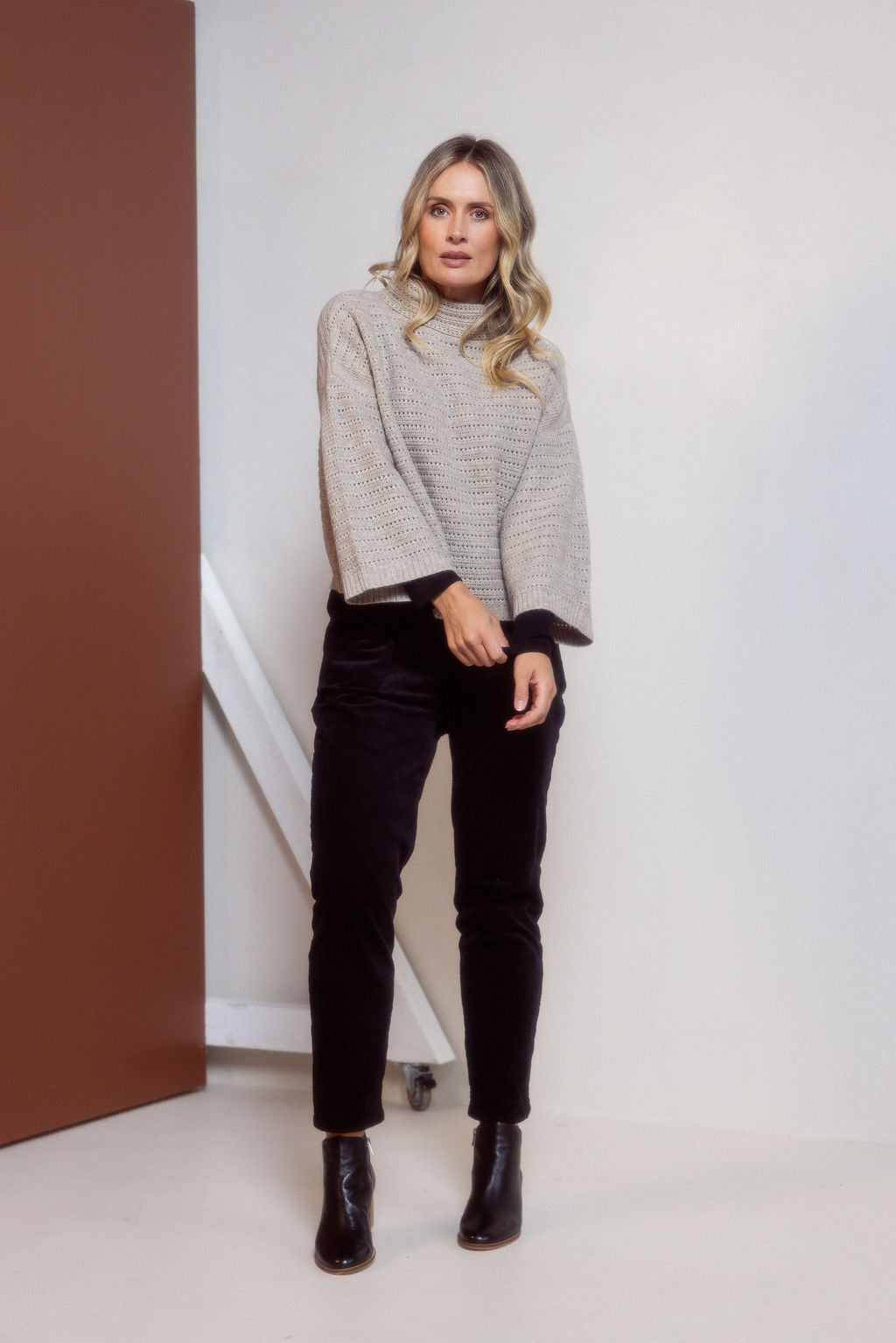 Woman wearing a See Saw Oat Marle pointelle sweater and polka dot shirt standing against a white background.